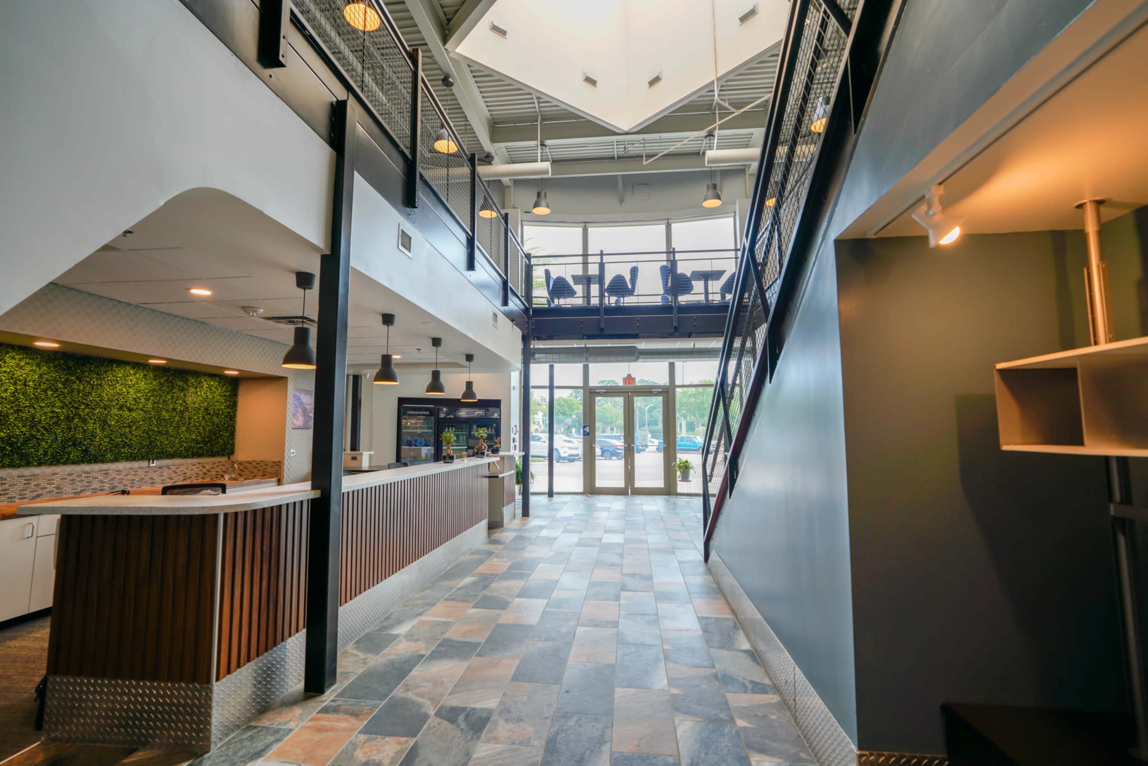 A modern lobby area with a reception desk on the left, green wall accents, and large windows allowing natural light to enter.