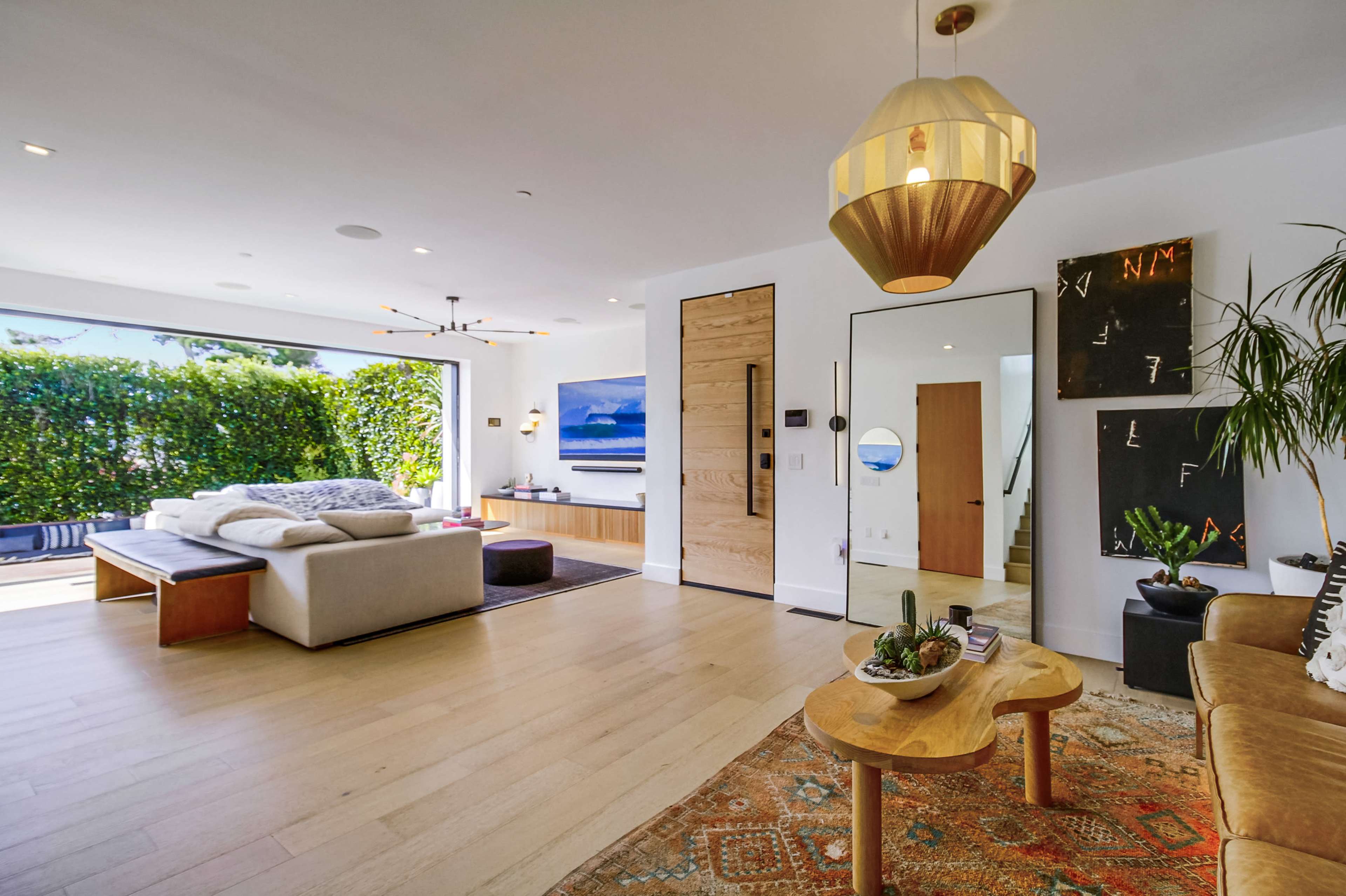 The image shows a modern living room with large windows, wooden flooring, and a blend of contemporary furniture and decor.