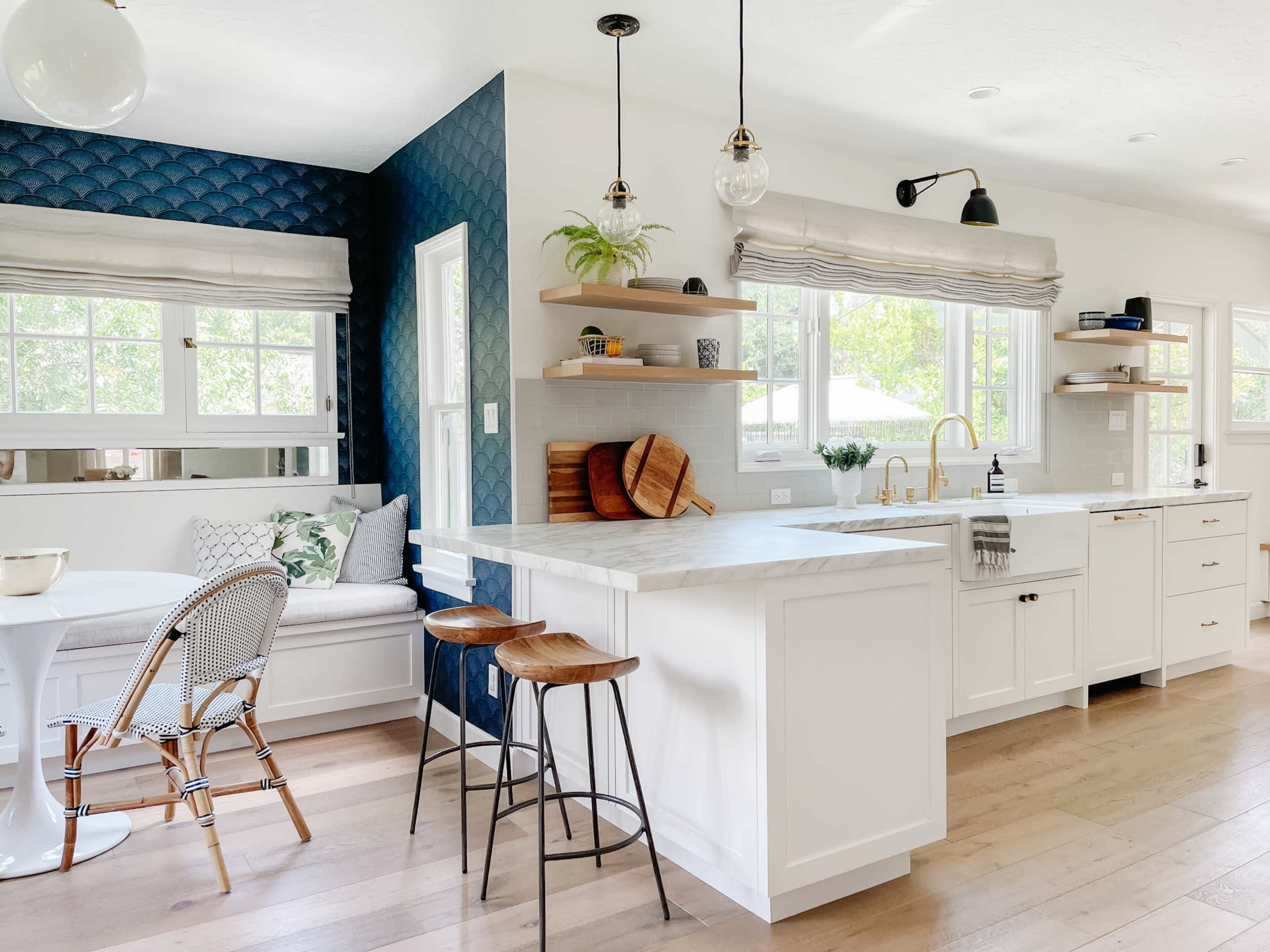 A modern kitchen features white cabinetry, a marble countertop island, and a blue accent wall with decorative shelving.