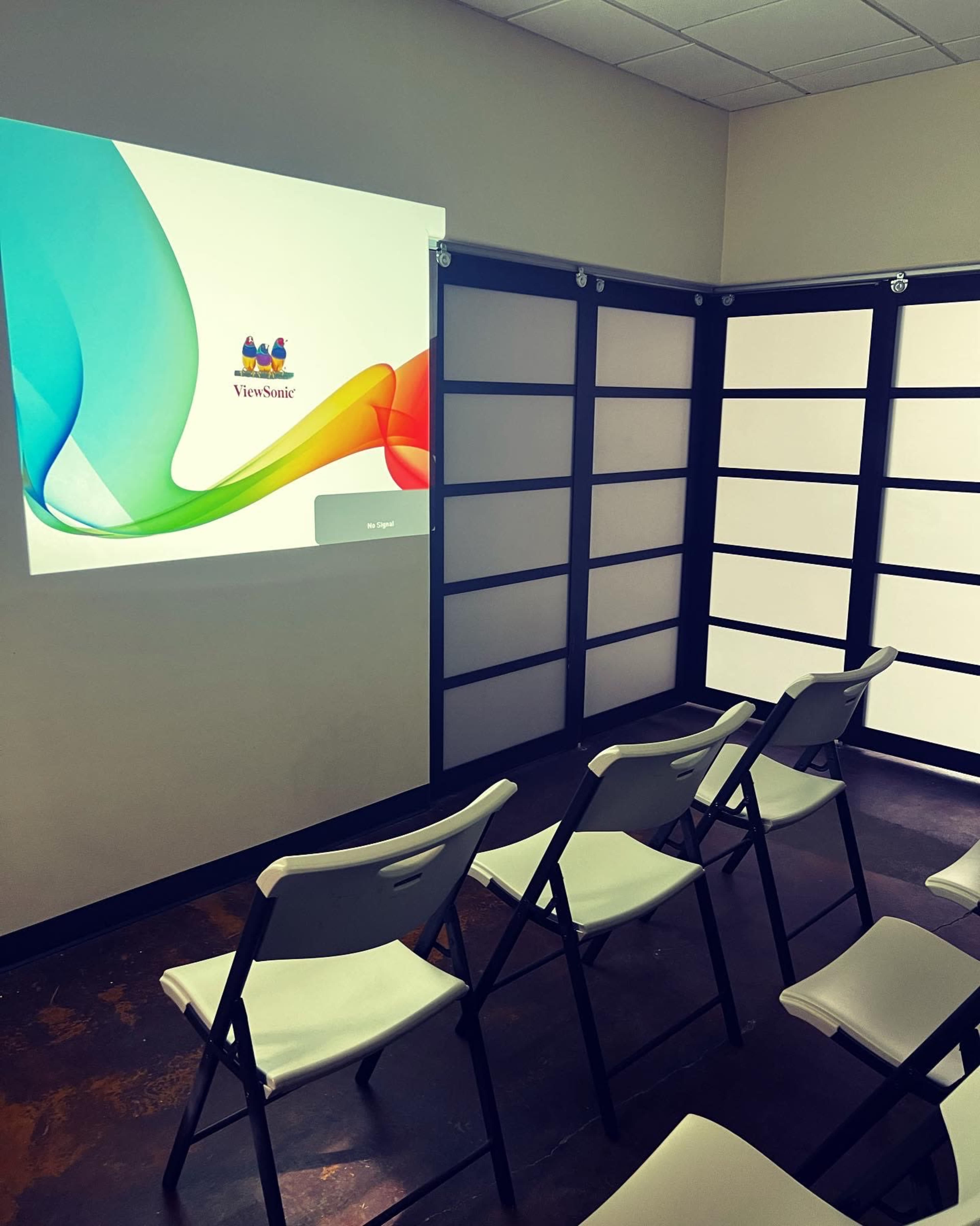 A projection screen is displayed on a wall in a room set up with several folding chairs facing it.