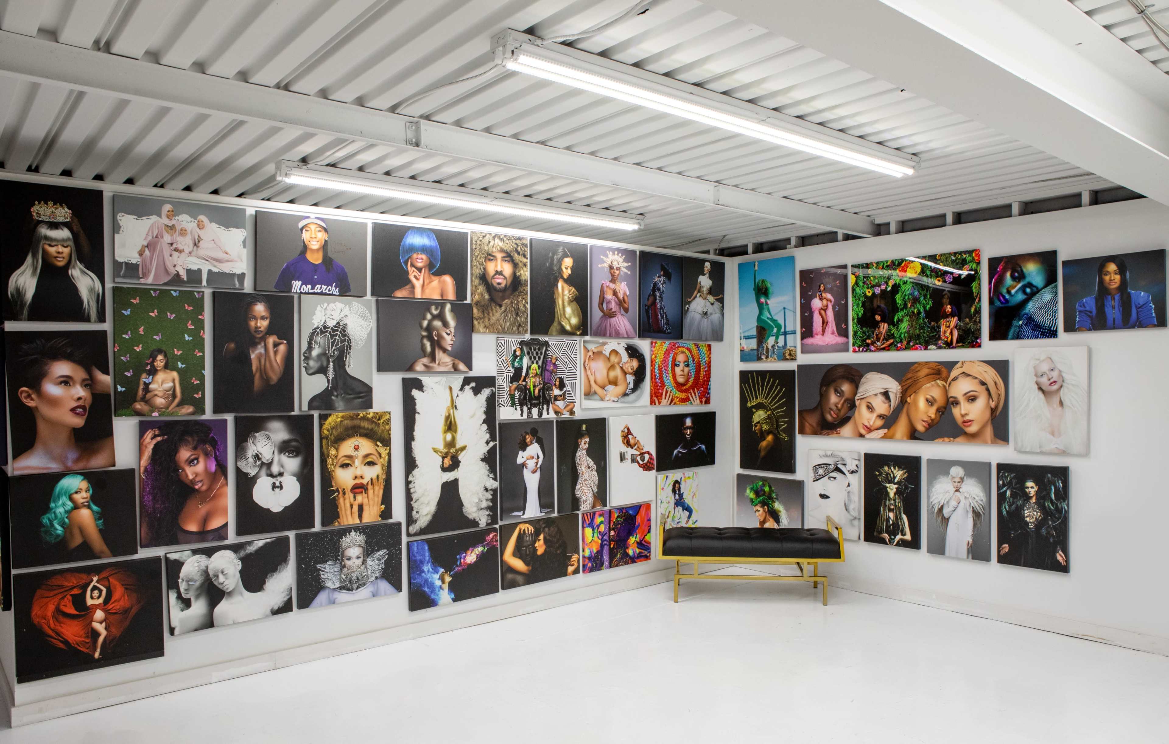 An art gallery wall filled with a diverse array of framed photographs, featuring various portraits and artistic displays, alongside a bench in the foreground.