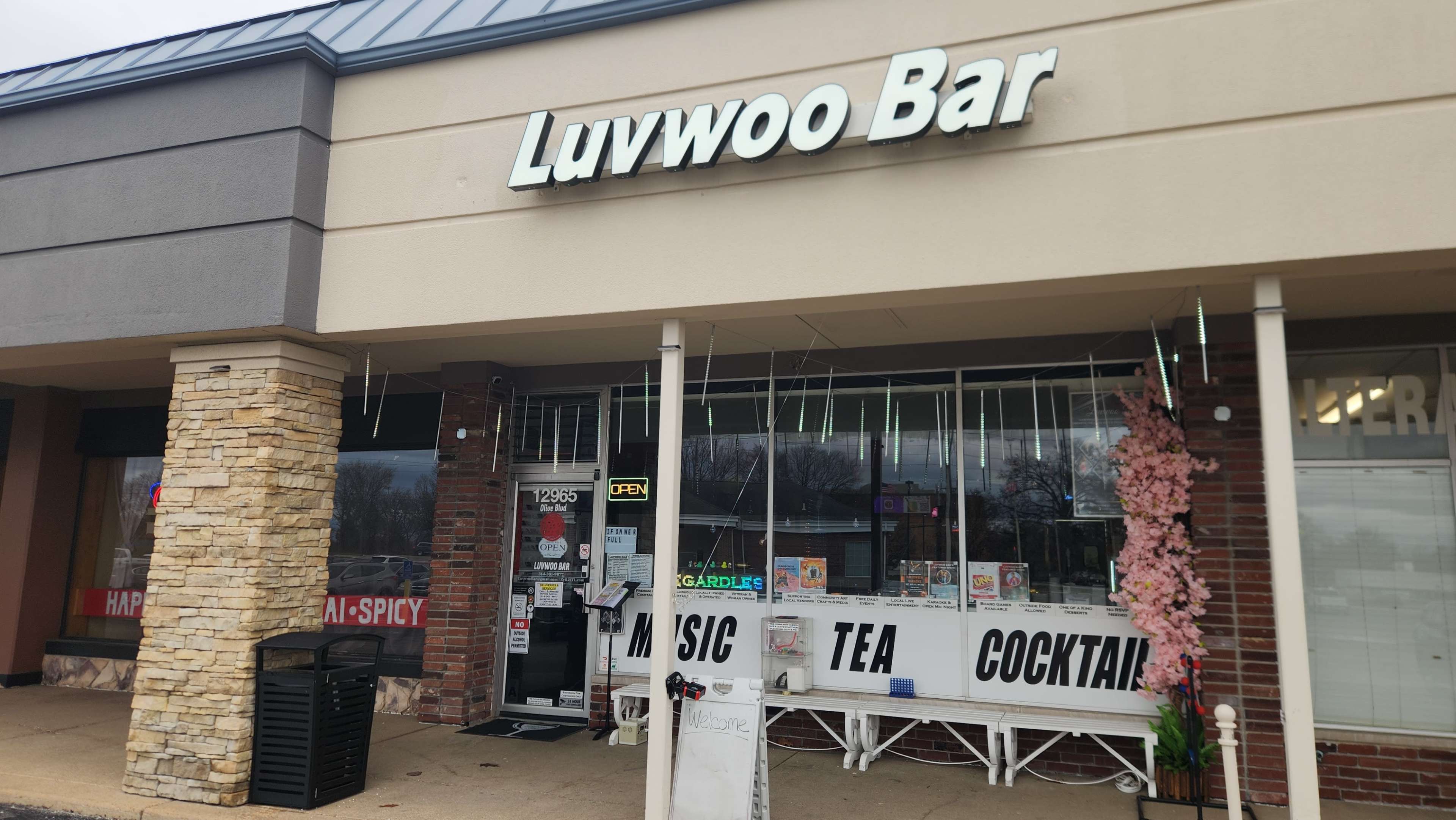 The image shows the exterior of Luvwoo Bar, featuring a large sign and a display of signage indicating services like music, tea, and cocktails.