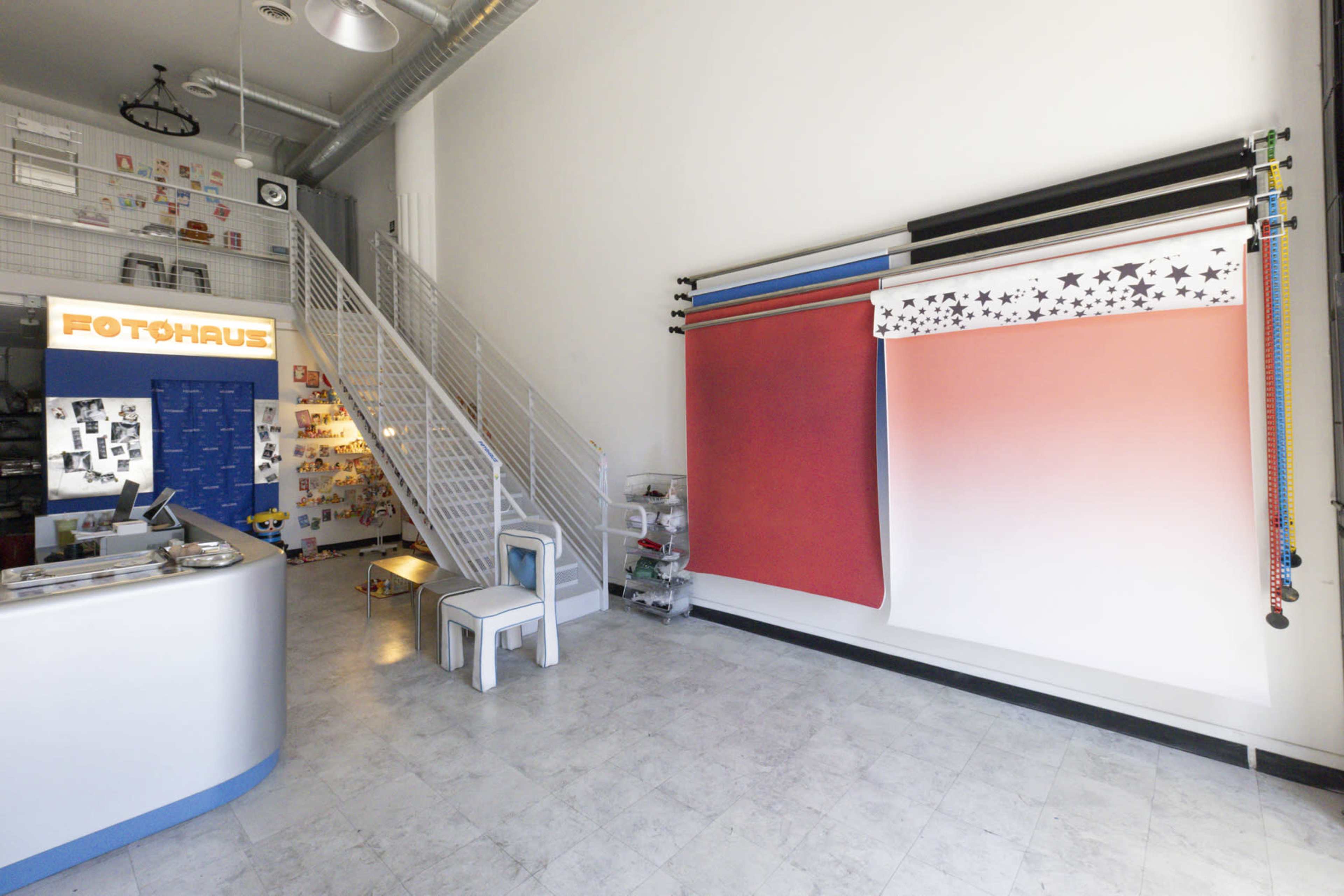 The image shows a photography studio with a reception area on the left and a wall of backdrop rolls in various colors on the right.