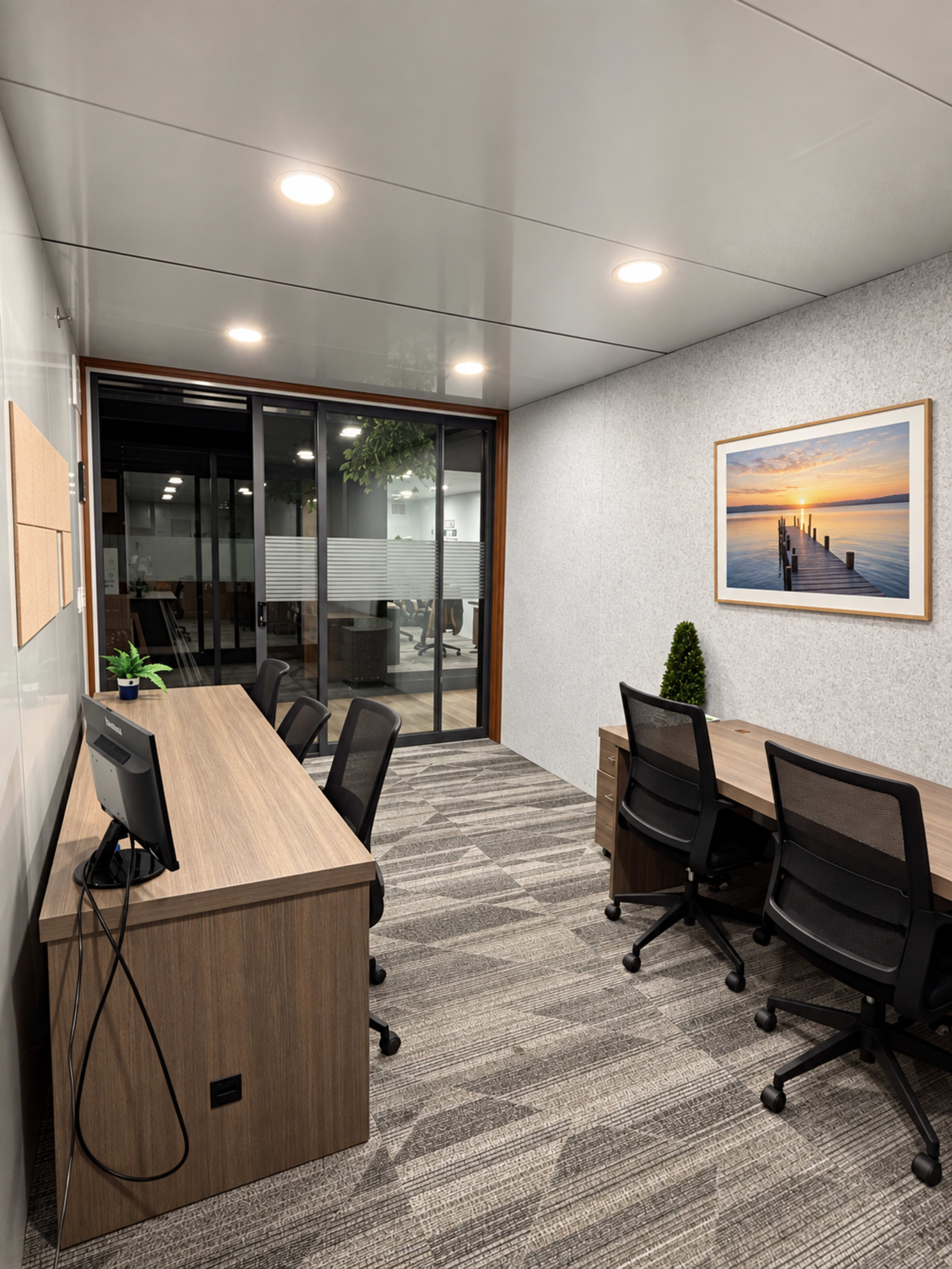 The image shows a modern office space with a reception area featuring wooden desks, ergonomic chairs, and large windows overlooking a meeting room.