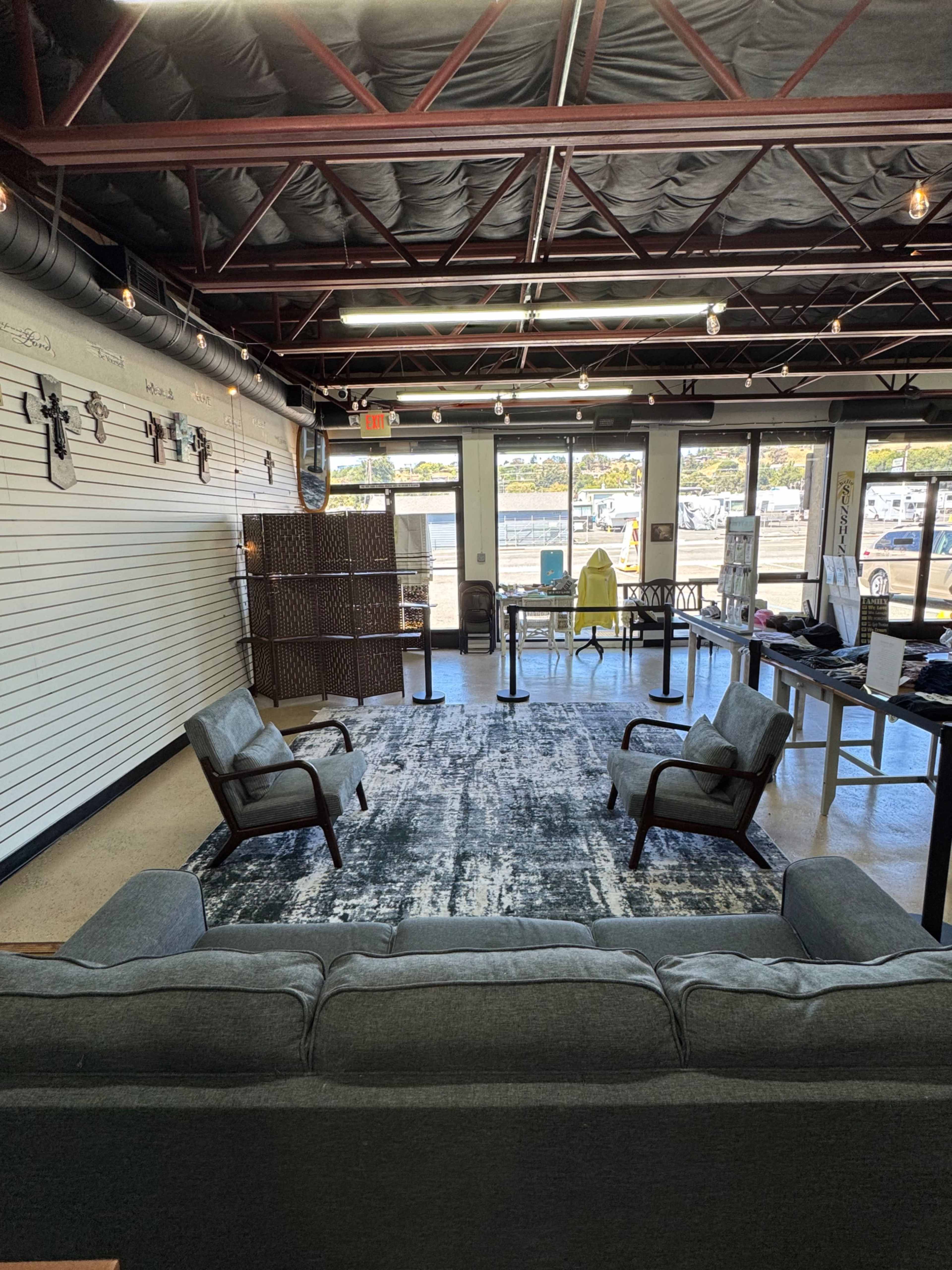 The image shows a modern interior space featuring two armchairs and a sofa arranged around a large rug, with large windows allowing natural light and a view of the outdoors.