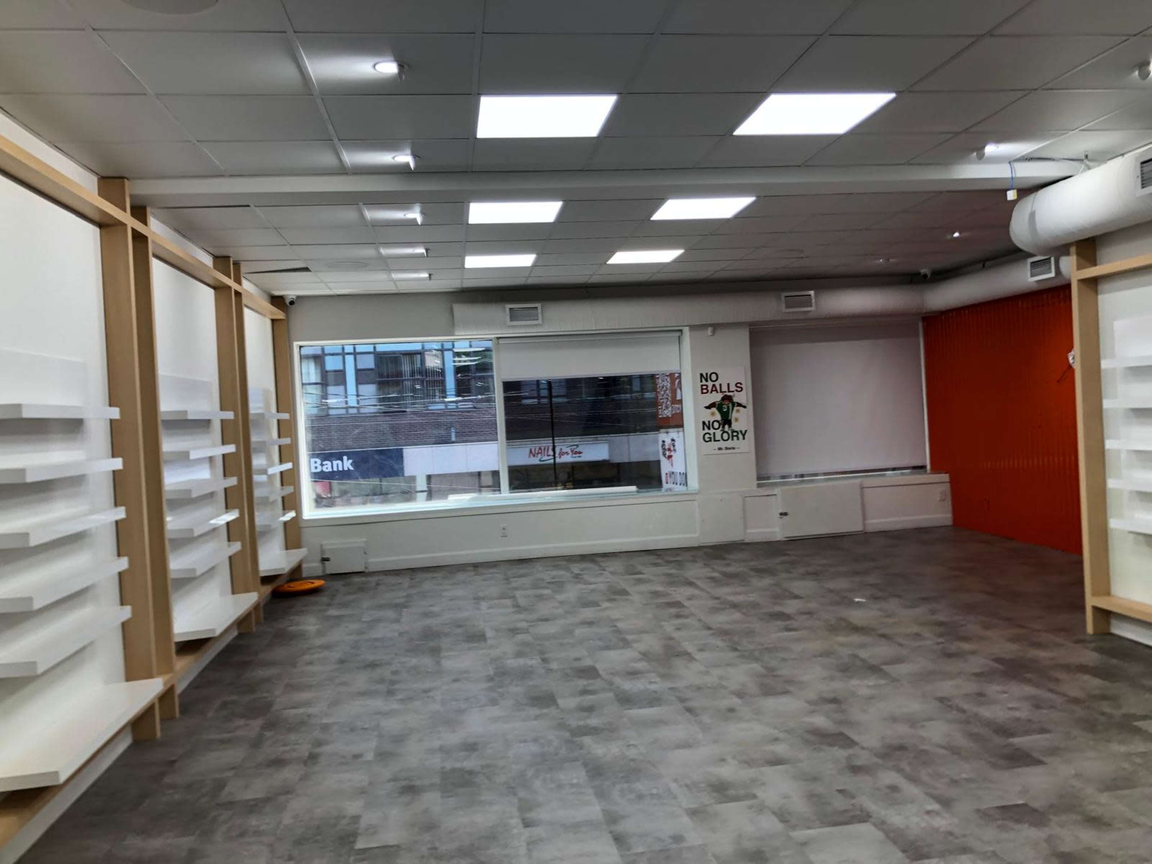 The image shows an empty retail space with shelves along the walls and large windows letting in natural light.