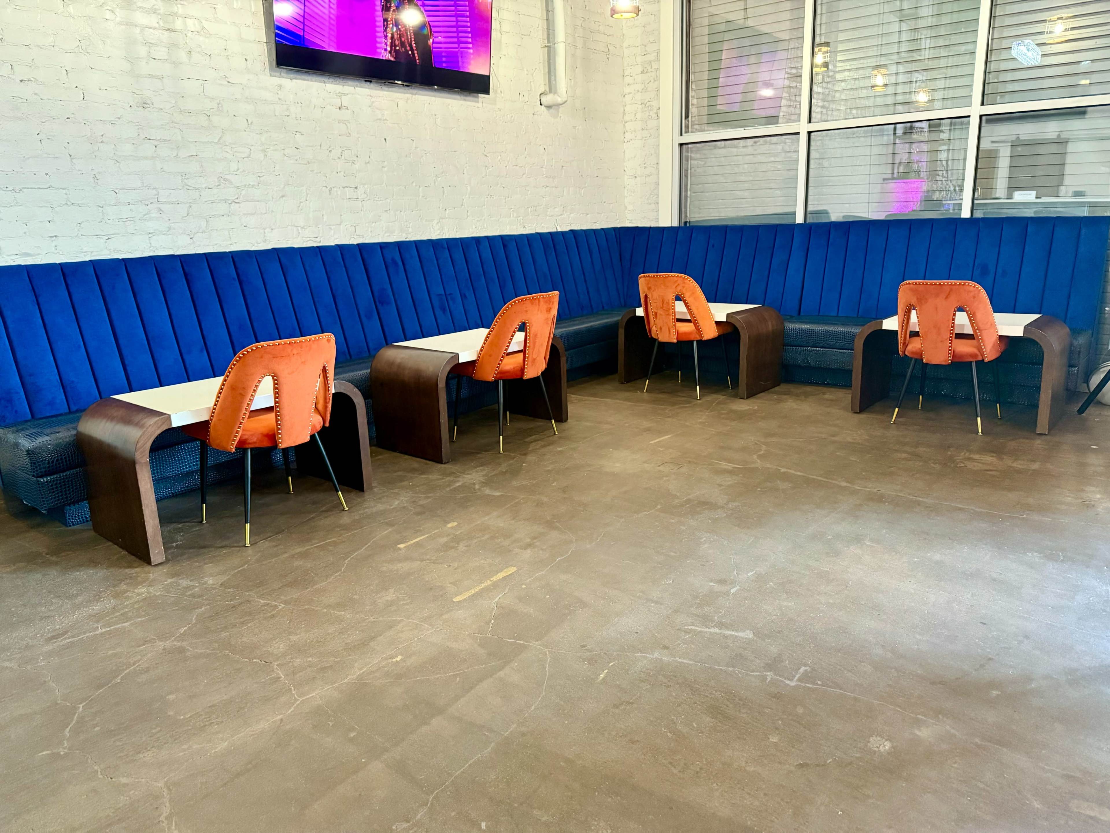 The image shows a seating area in a modern space with blue upholstered benches and orange chairs at small tables.