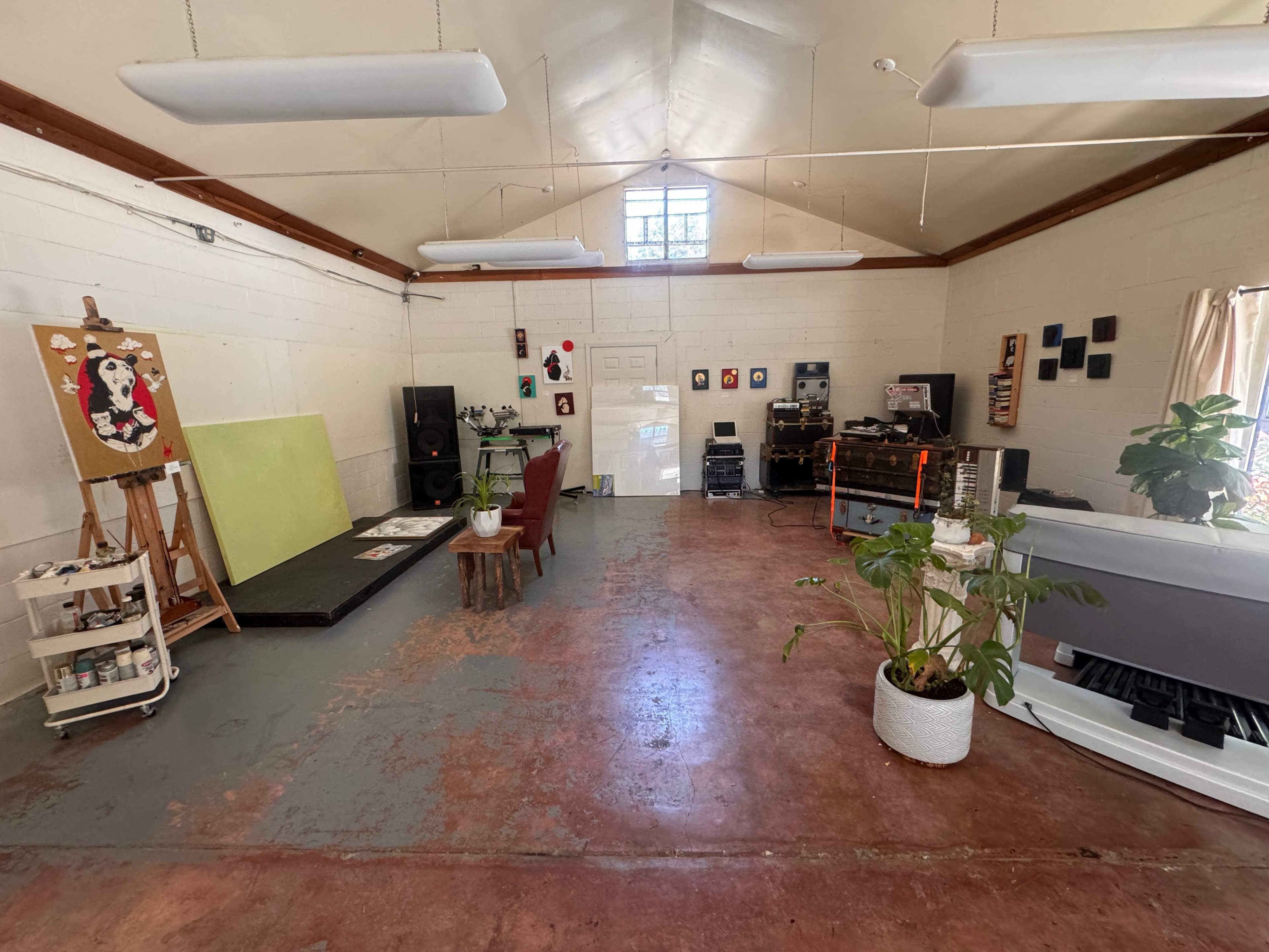 A spacious art studio with easels, artwork on the walls, and various plants placed throughout the room.