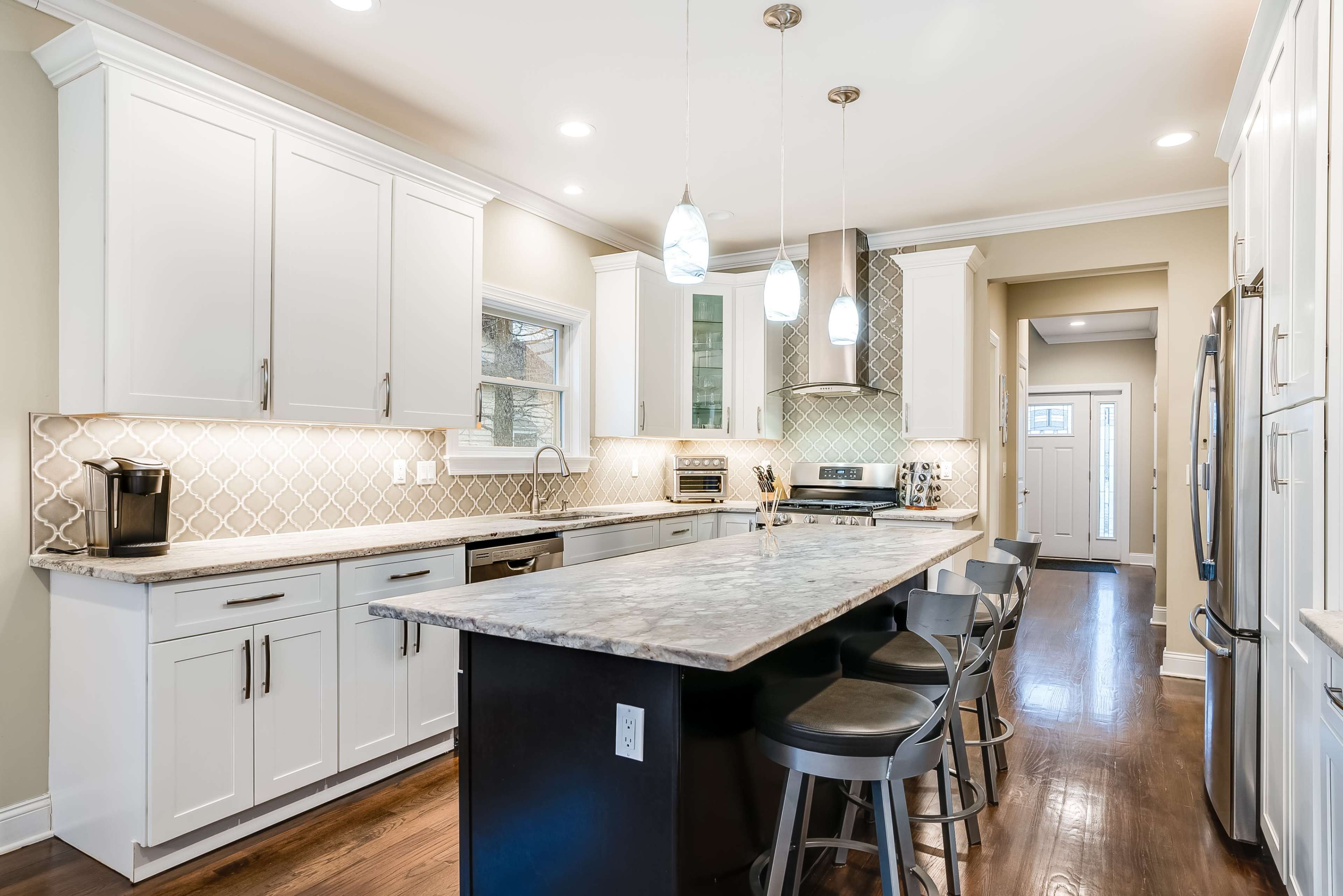 A modern kitchen features white cabinetry, gray countertops, stainless steel appliances, and a large island with seating.