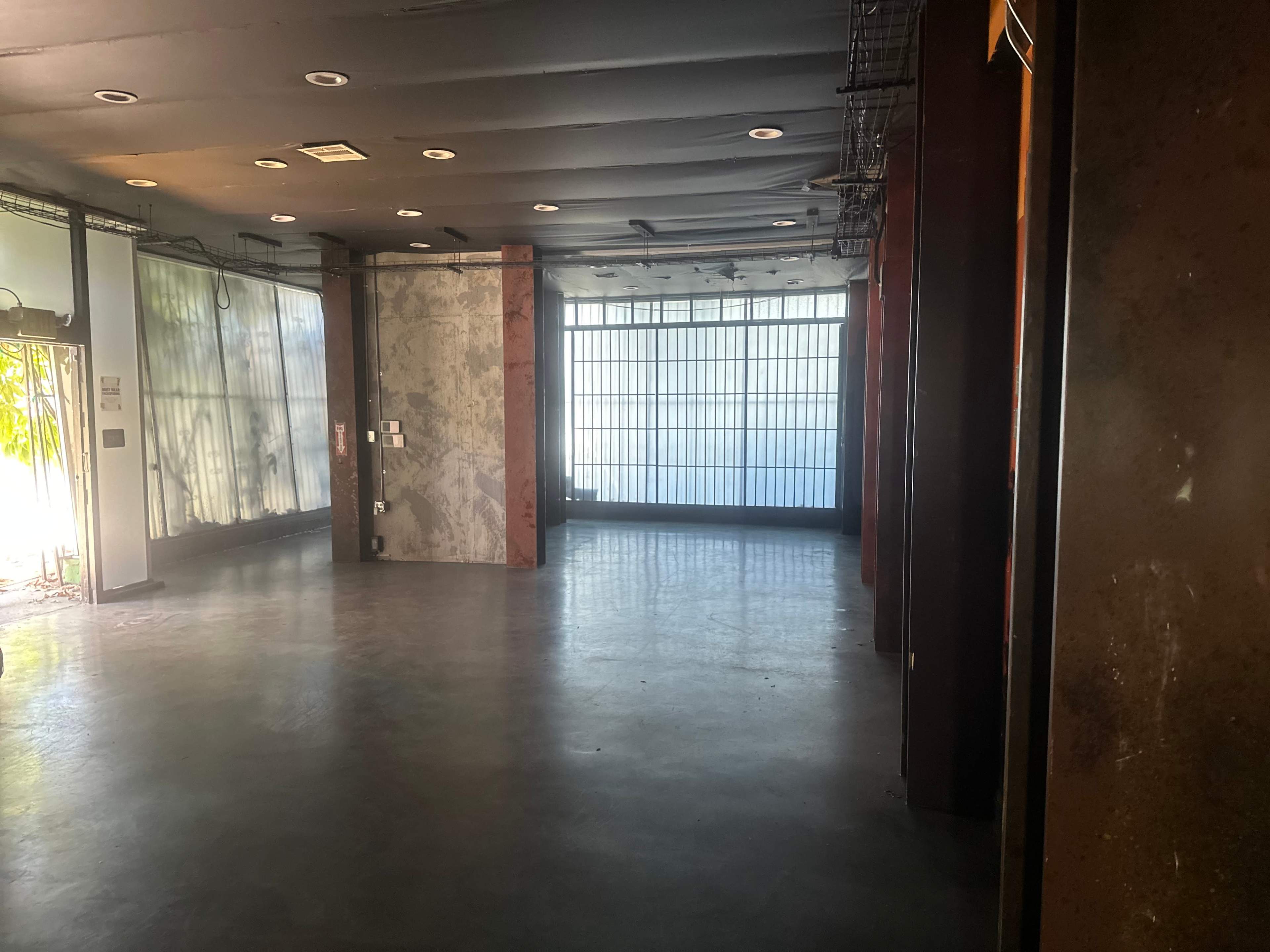 The image shows an empty, industrial-style interior with large windows and concrete flooring.