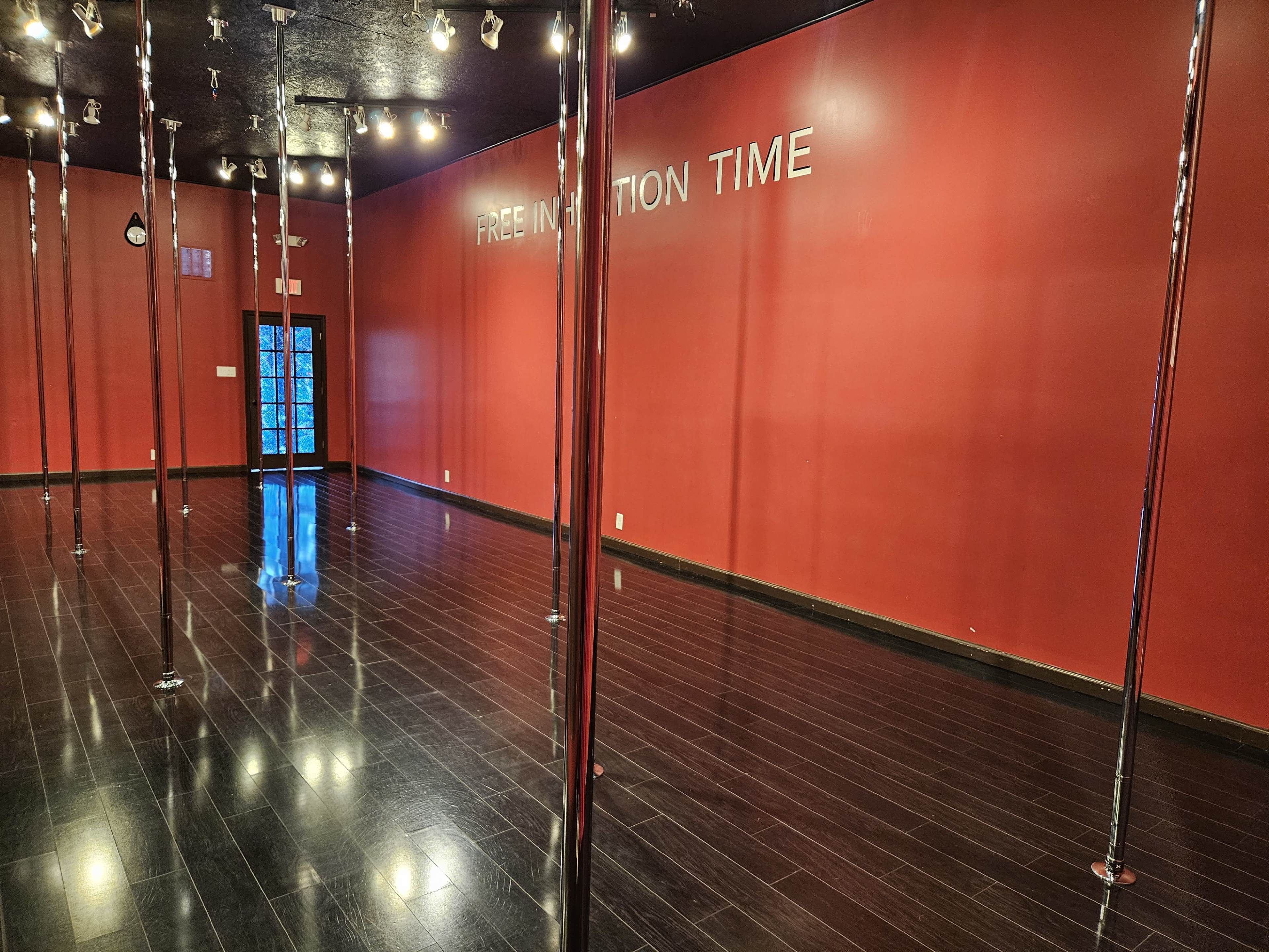 An empty room with polished wooden floors, red walls, and several metal poles reflecting overhead lights.