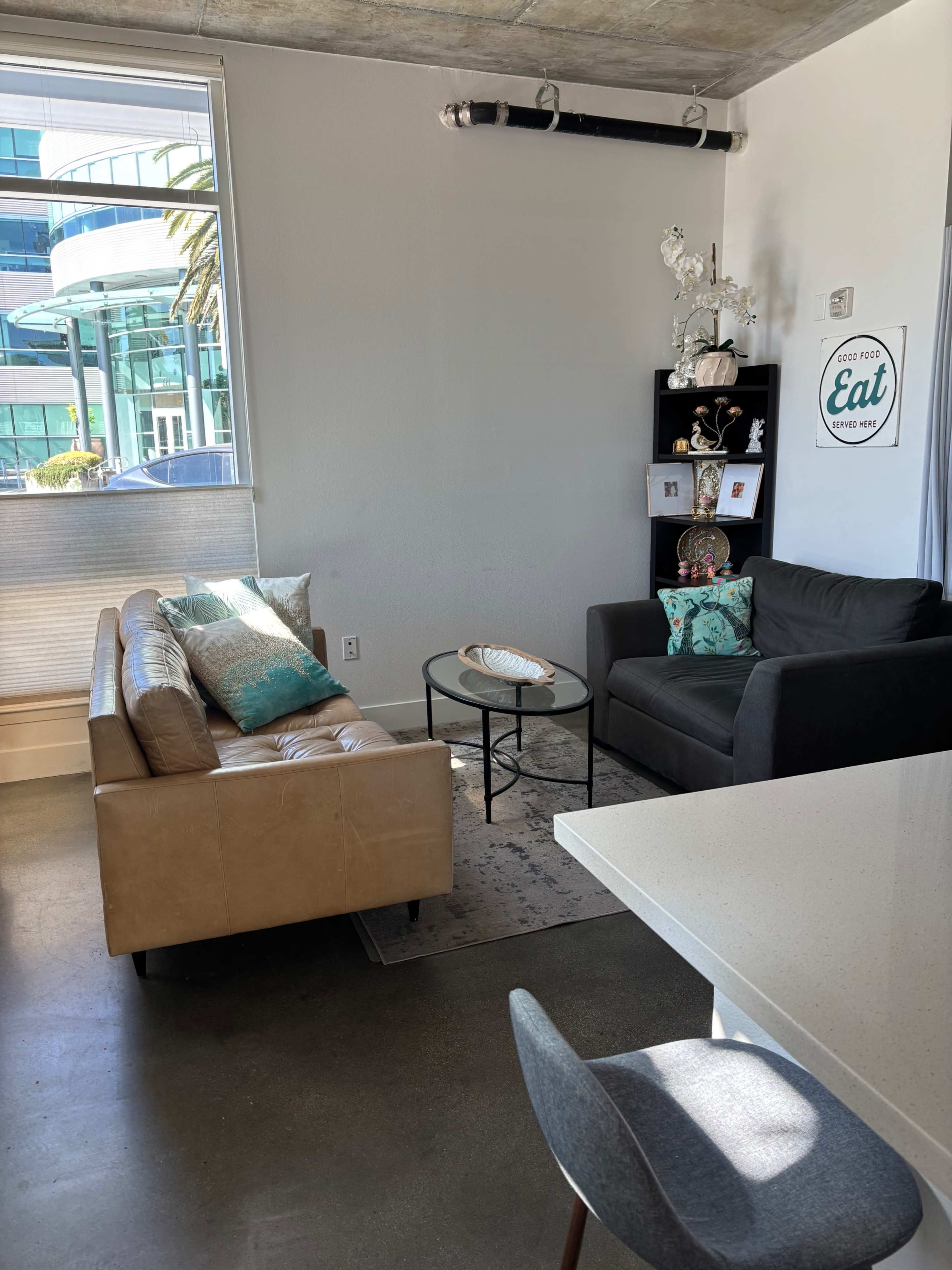 The image shows a modern living space featuring a tan leather sofa, a black chair, a round coffee table, and decorative shelves.