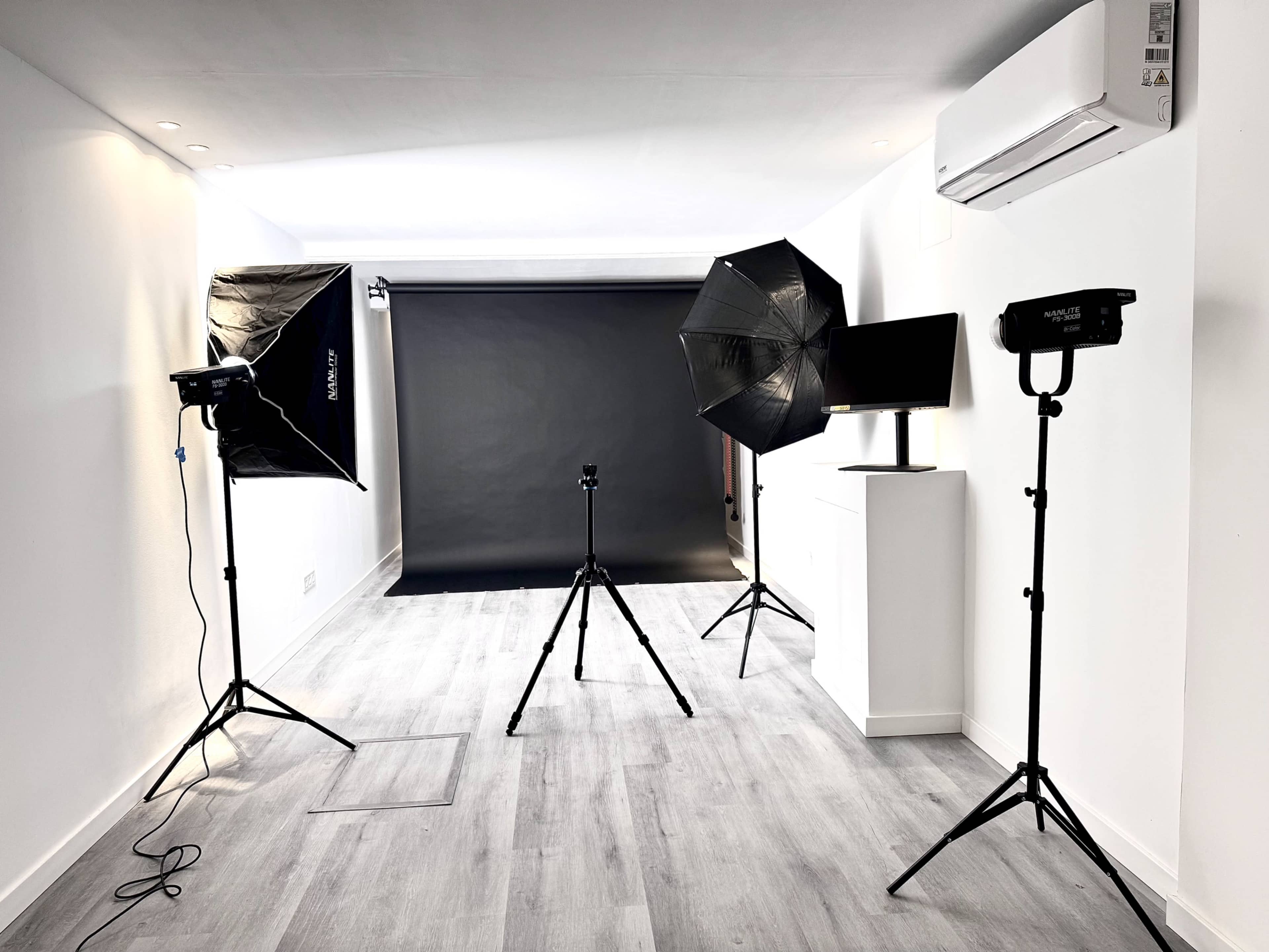 The image shows a photography studio equipped with two softbox lights, a reflector, a camera tripod, and a dark backdrop.