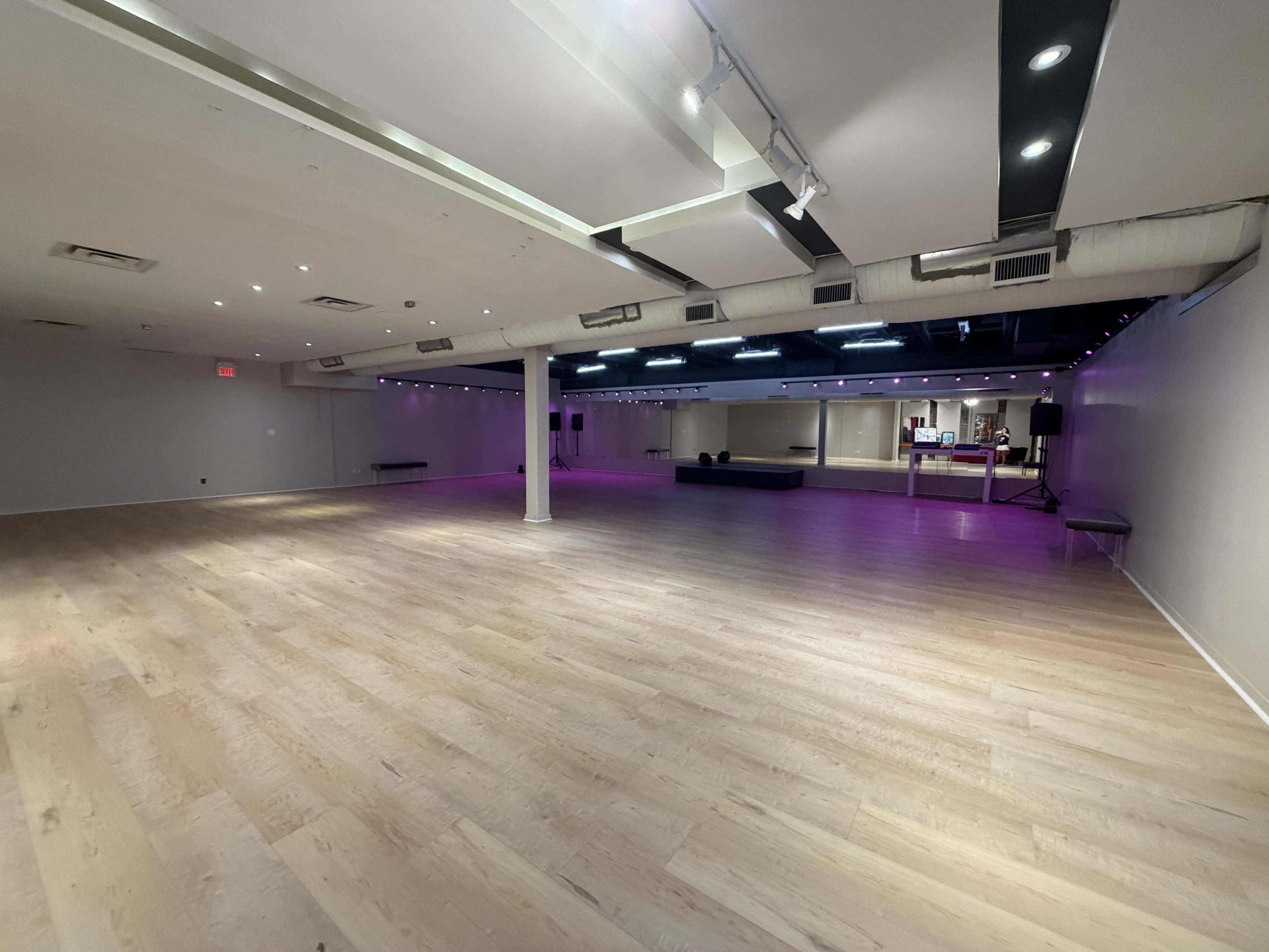 The image shows a spacious dance studio with polished wooden floors and purple lighting along the walls.