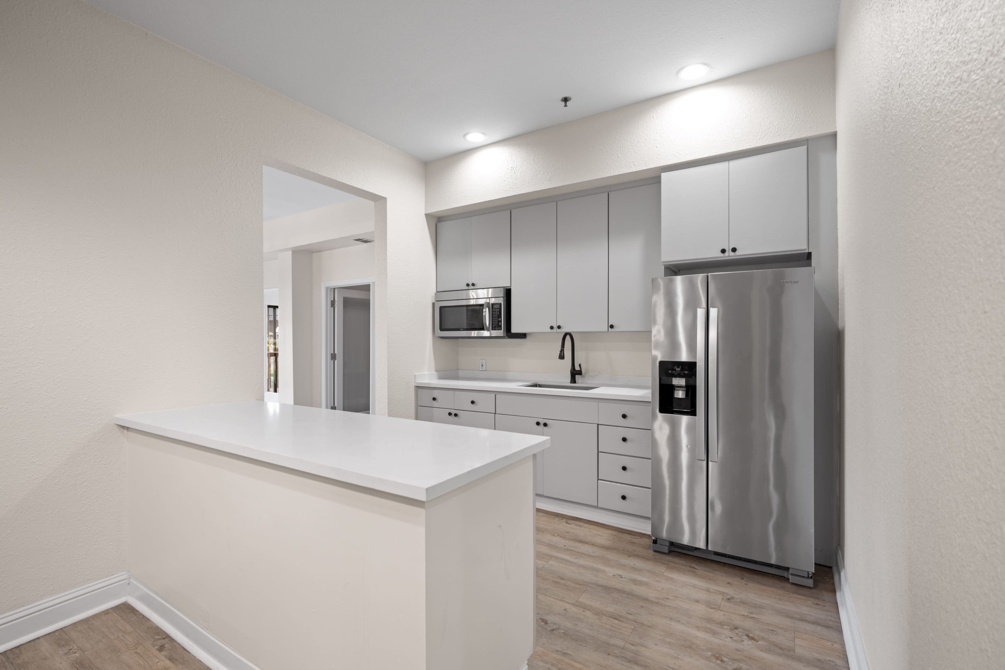 The image shows a modern kitchen featuring white cabinets, stainless steel appliances, and a light-colored countertop.