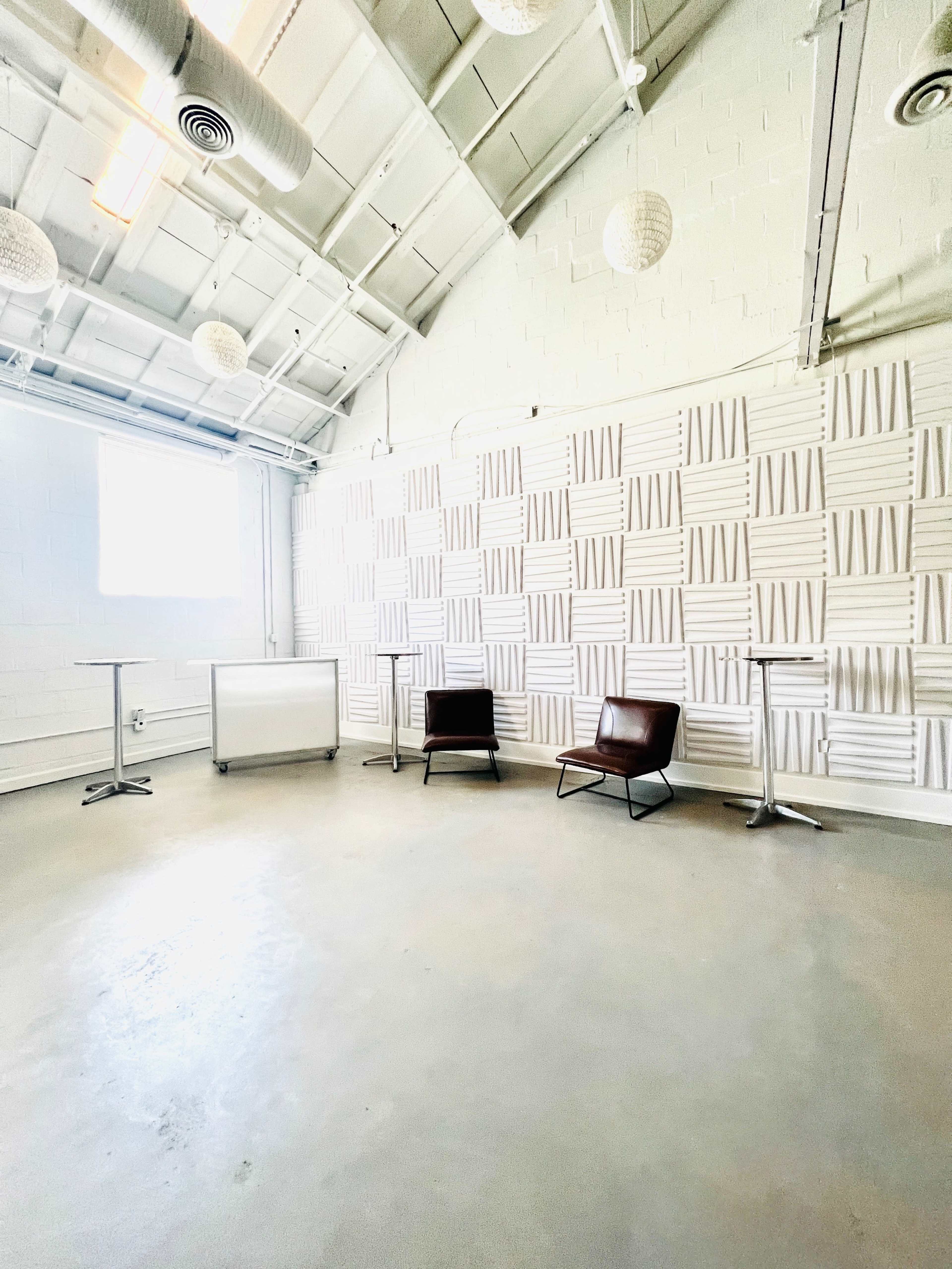 A bright, empty room with a textured wall, two brown chairs, and small tables.