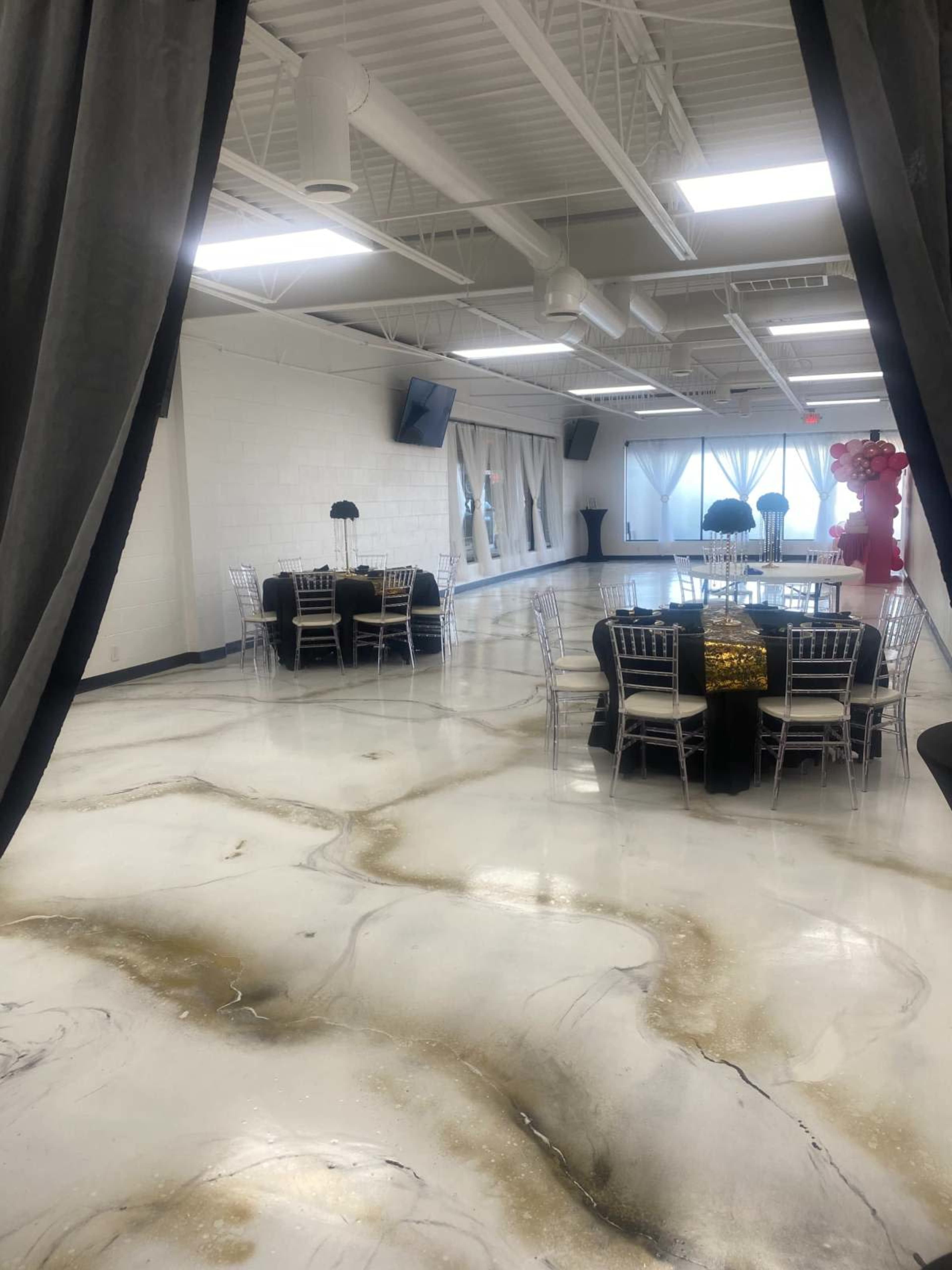 A spacious event hall with polished marble flooring and multiple dining setups, including black tables and chairs with decorative elements.