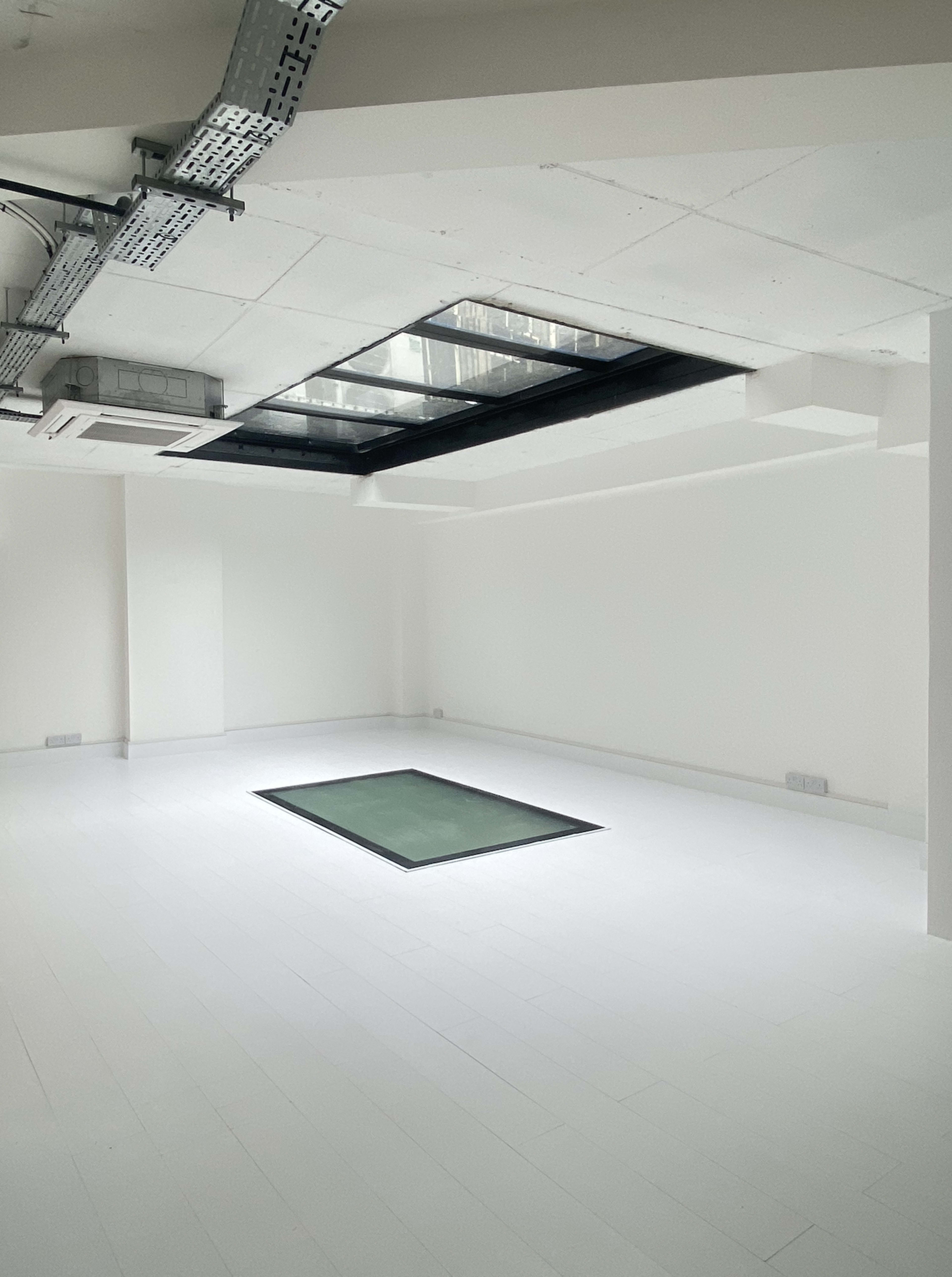 A minimalist white room with a rectangular opening in the ceiling and a glass panel on the floor.