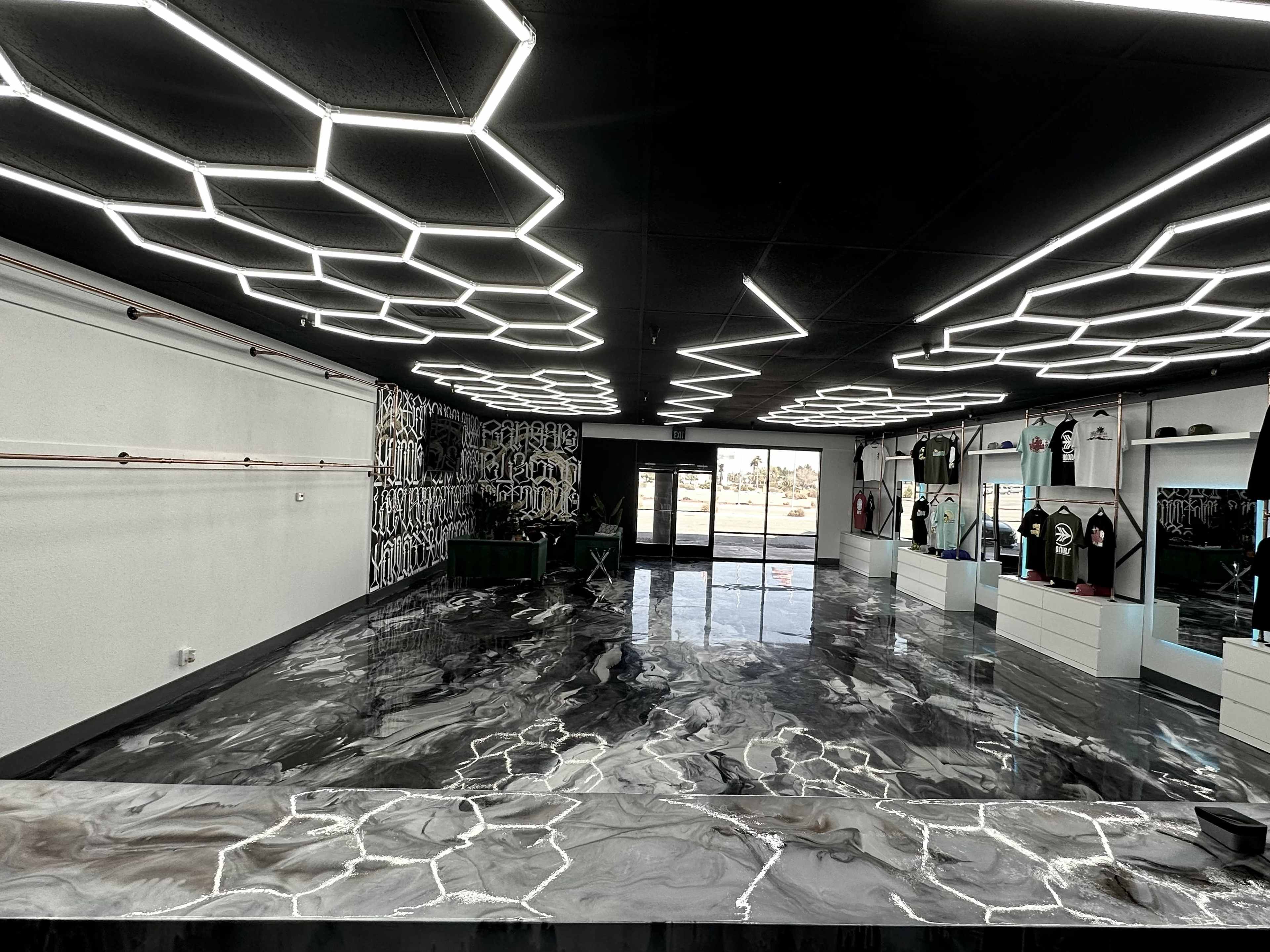 A modern retail space featuring sleek, geometric LED lighting, a polished marble floor, and displays of clothing along the walls.