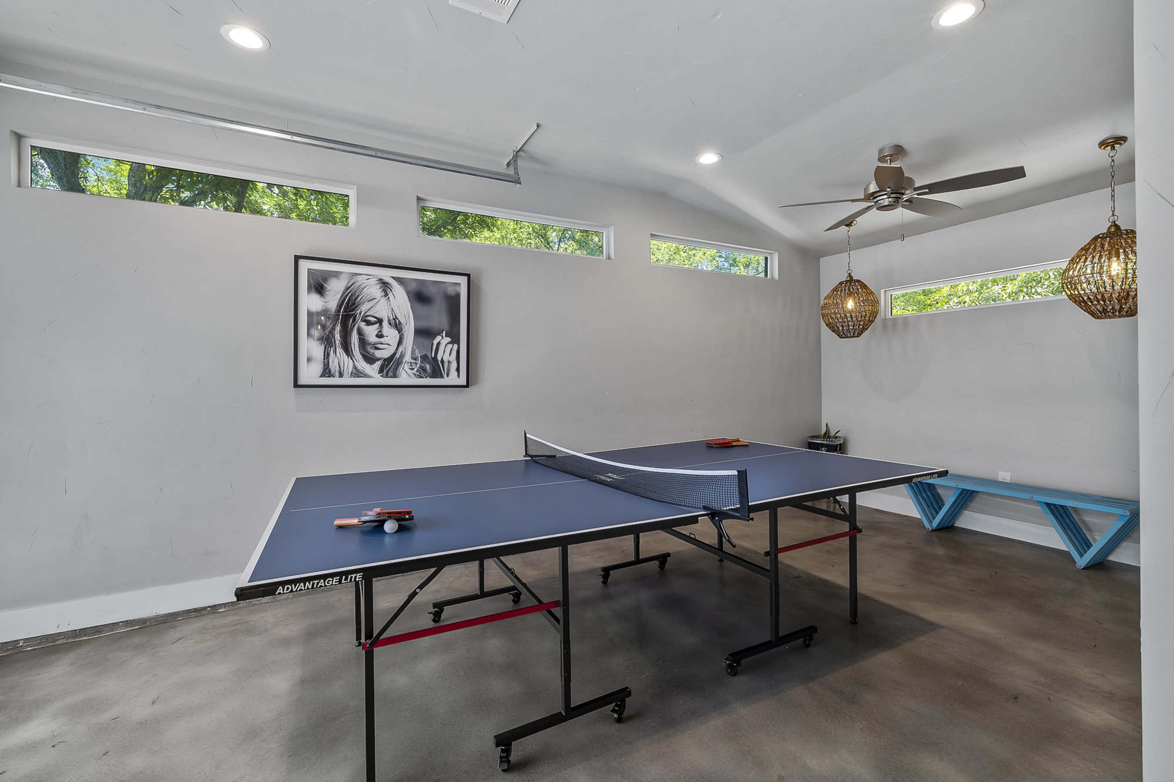 A room features a ping pong table, natural light from narrow windows, and decorative pendant lights.