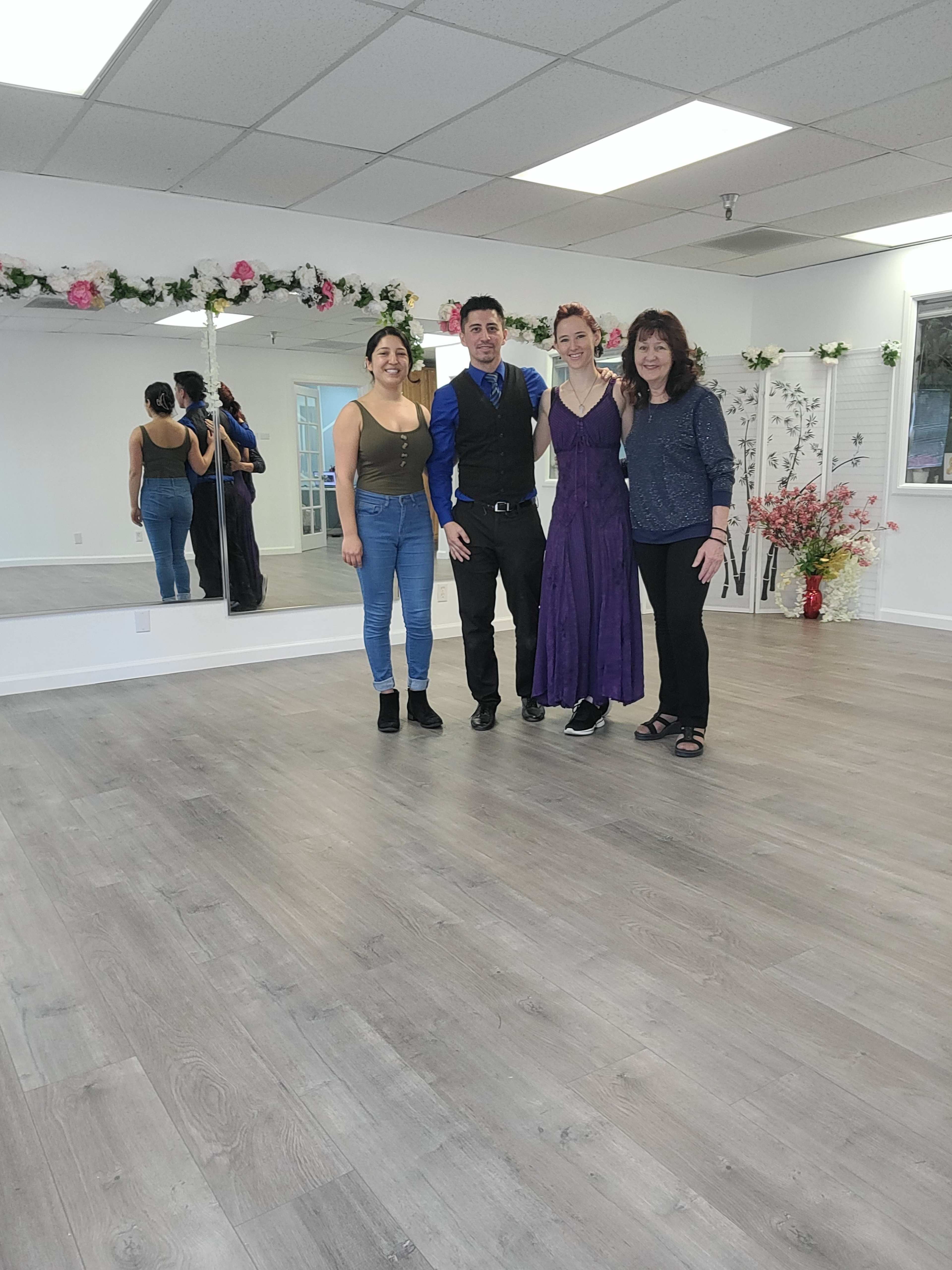 Three individuals stand in a bright dance studio with mirrored walls and floral decorations.
