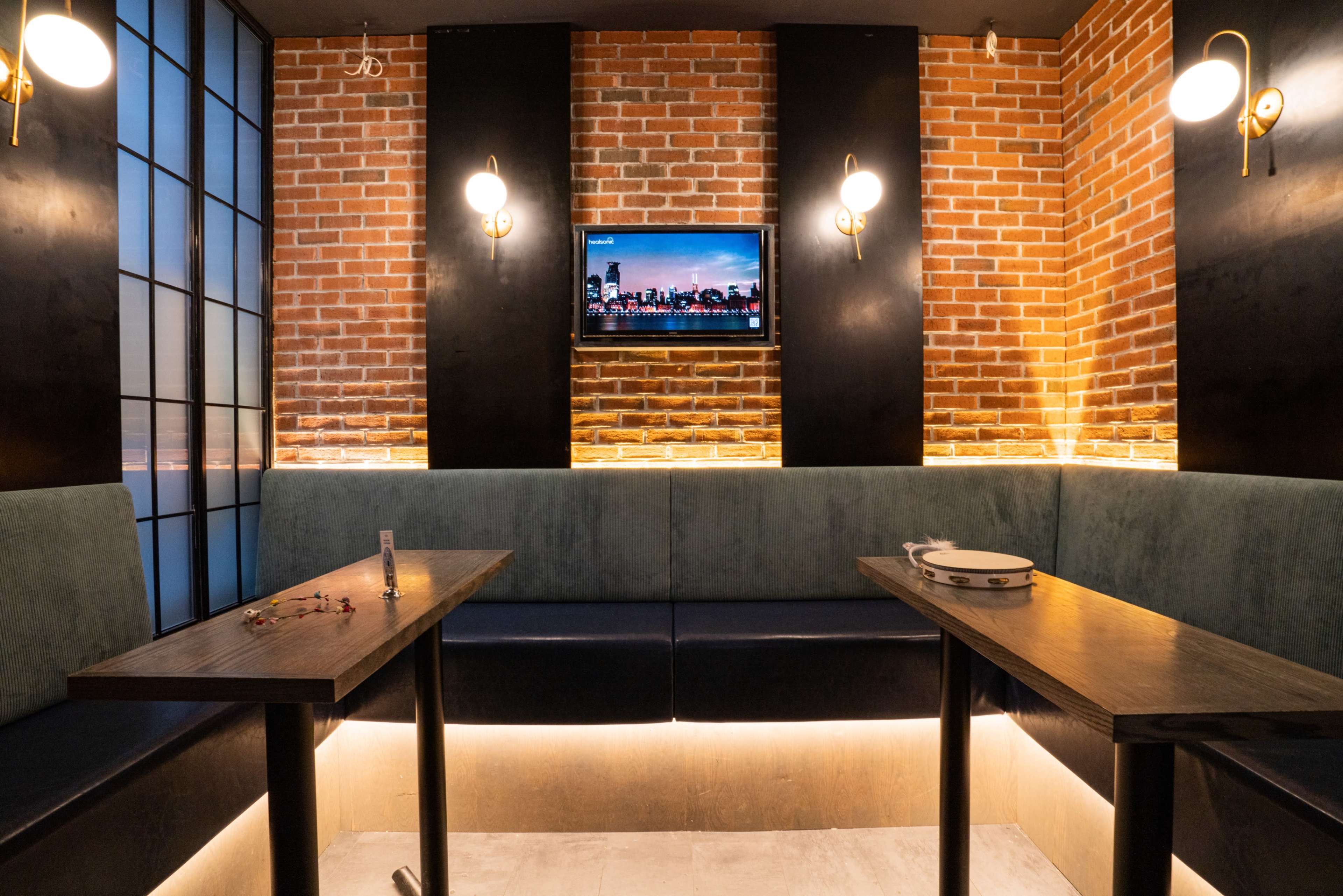 A modern restaurant booth with brick walls, low lighting, and a television mounted on the wall.