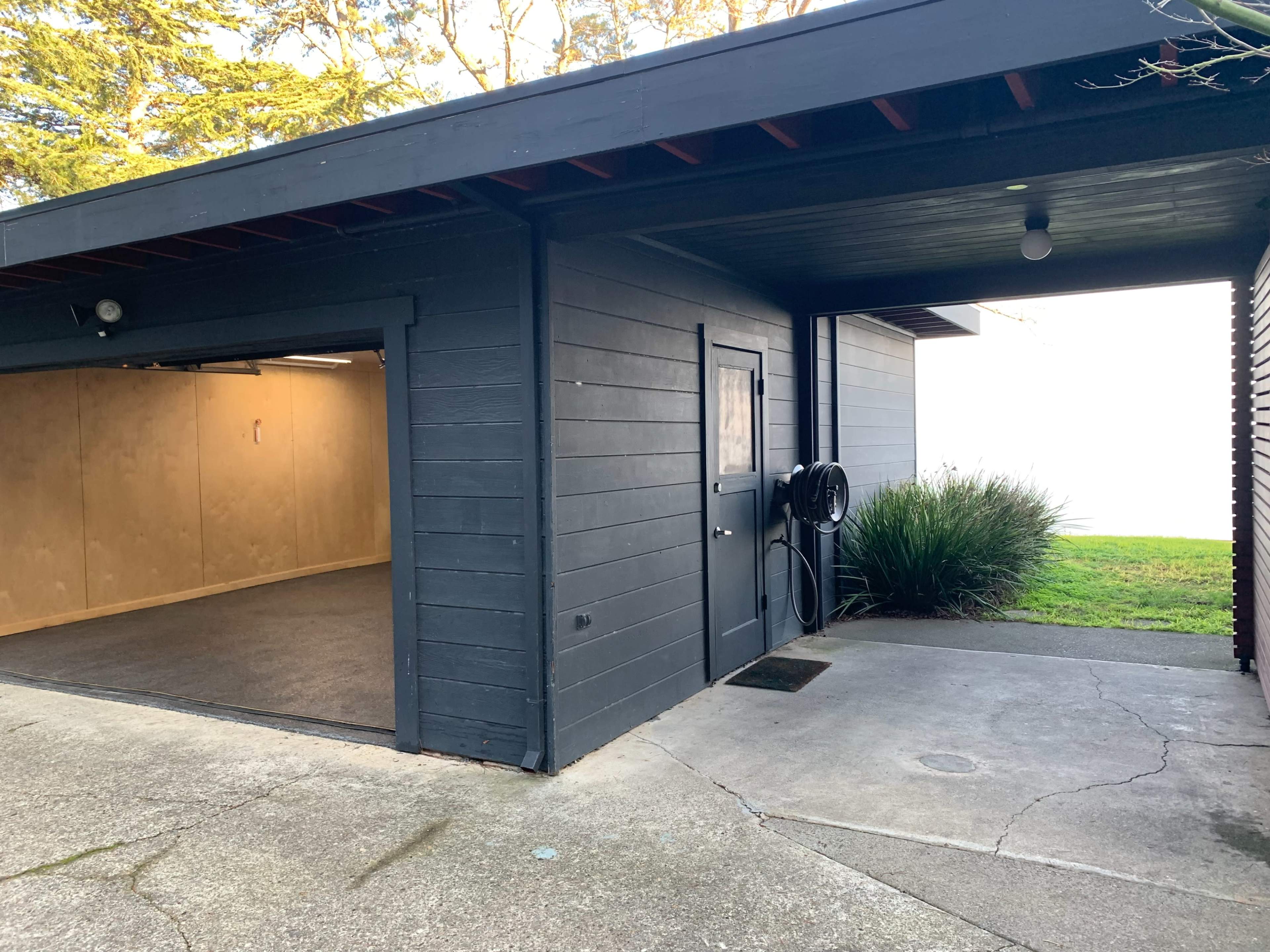 A dark-colored garage with a side door, situated beside a concrete driveway and a patch of grass.