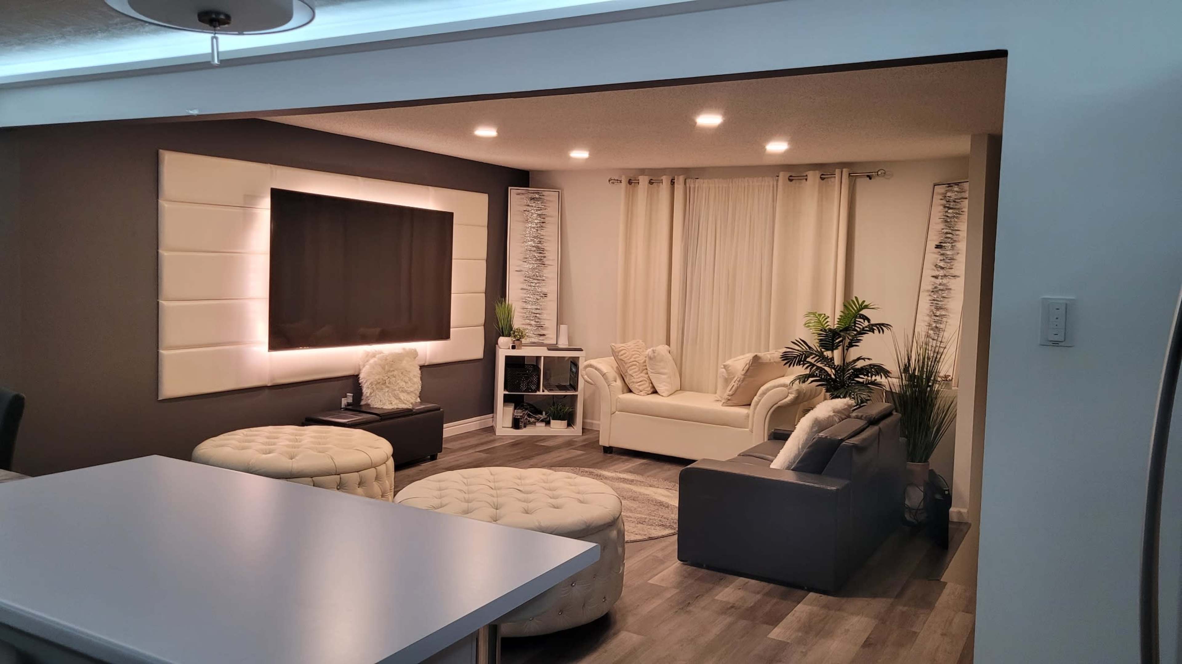 A modern living room with a large television mounted on the wall, two light-colored sofas, and decorative plants.
