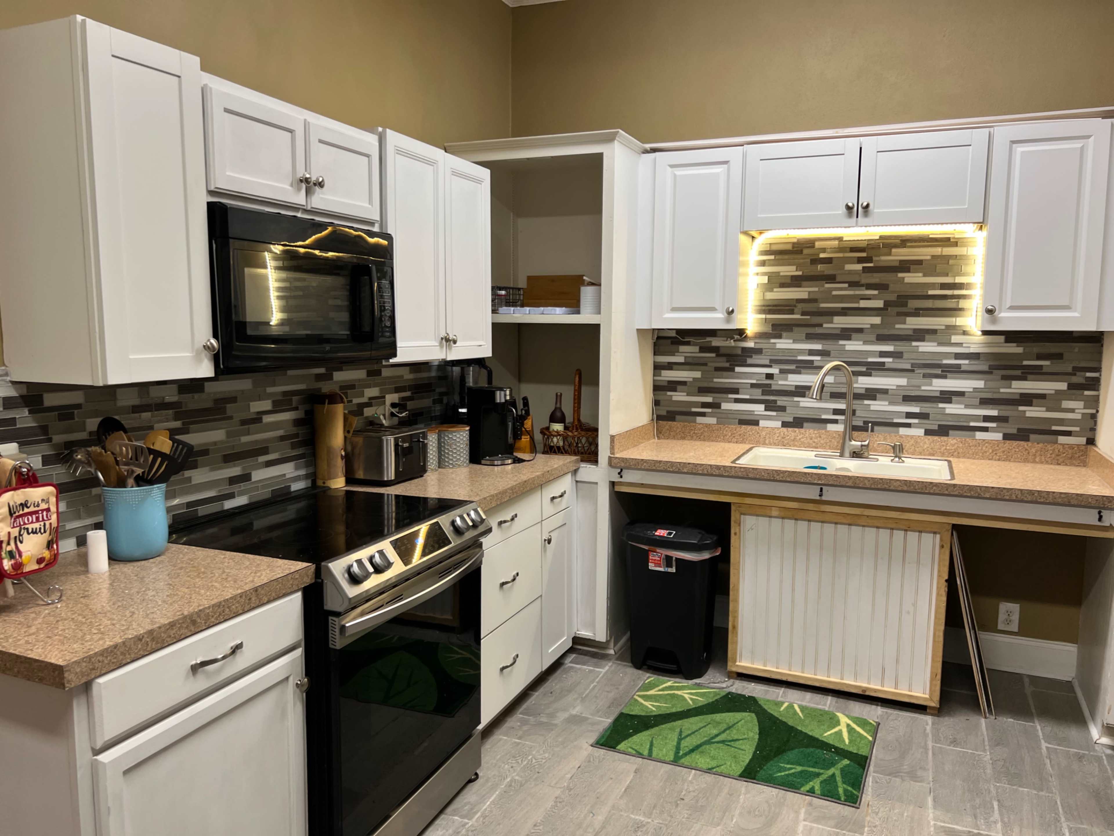 A modern kitchen features white cabinets, a gray tiled backsplash, stainless steel appliances, and a brown countertop with a sink and a dish rack.