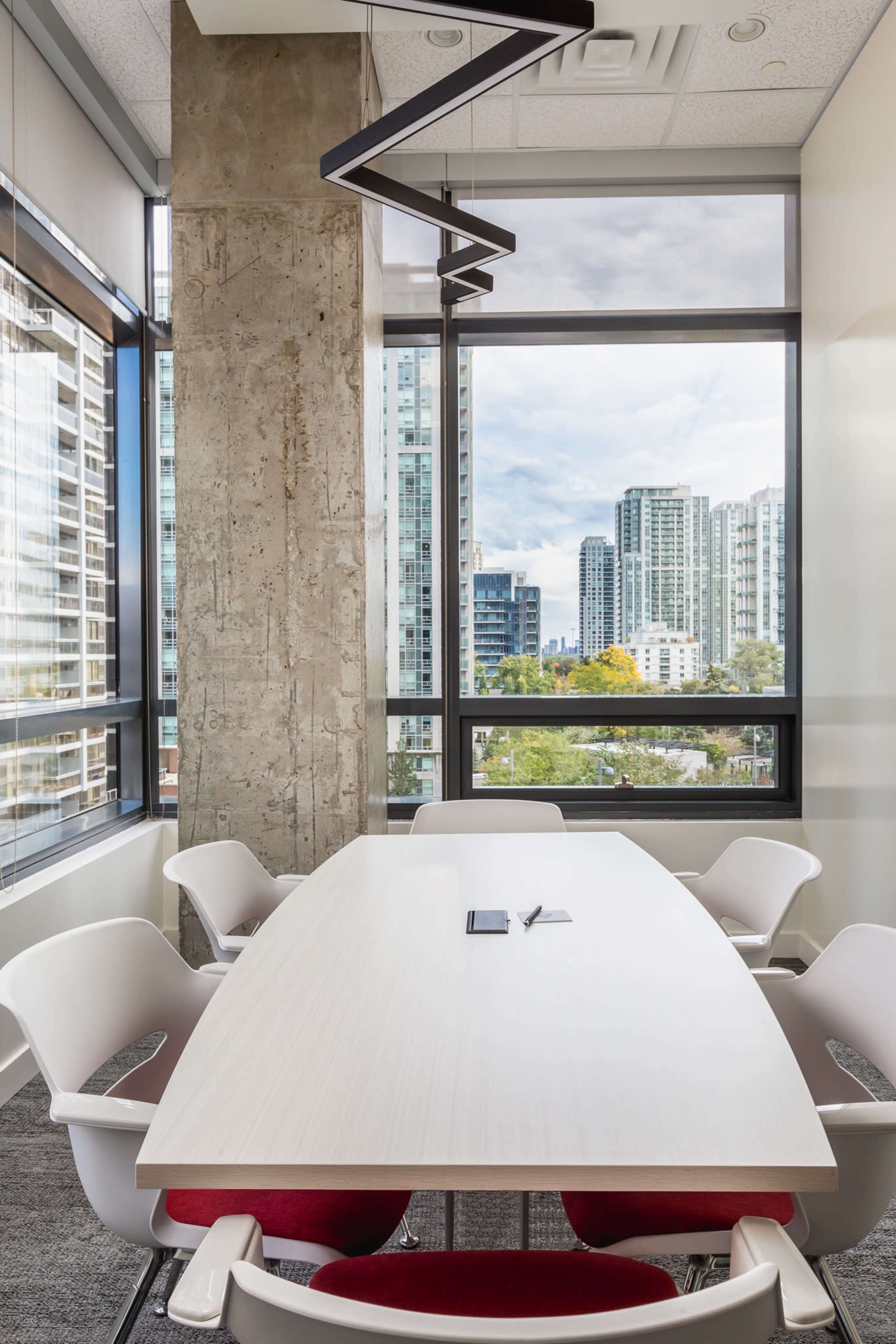 A modern conference room features a long white table surrounded by white chairs, with large windows displaying a city skyline.