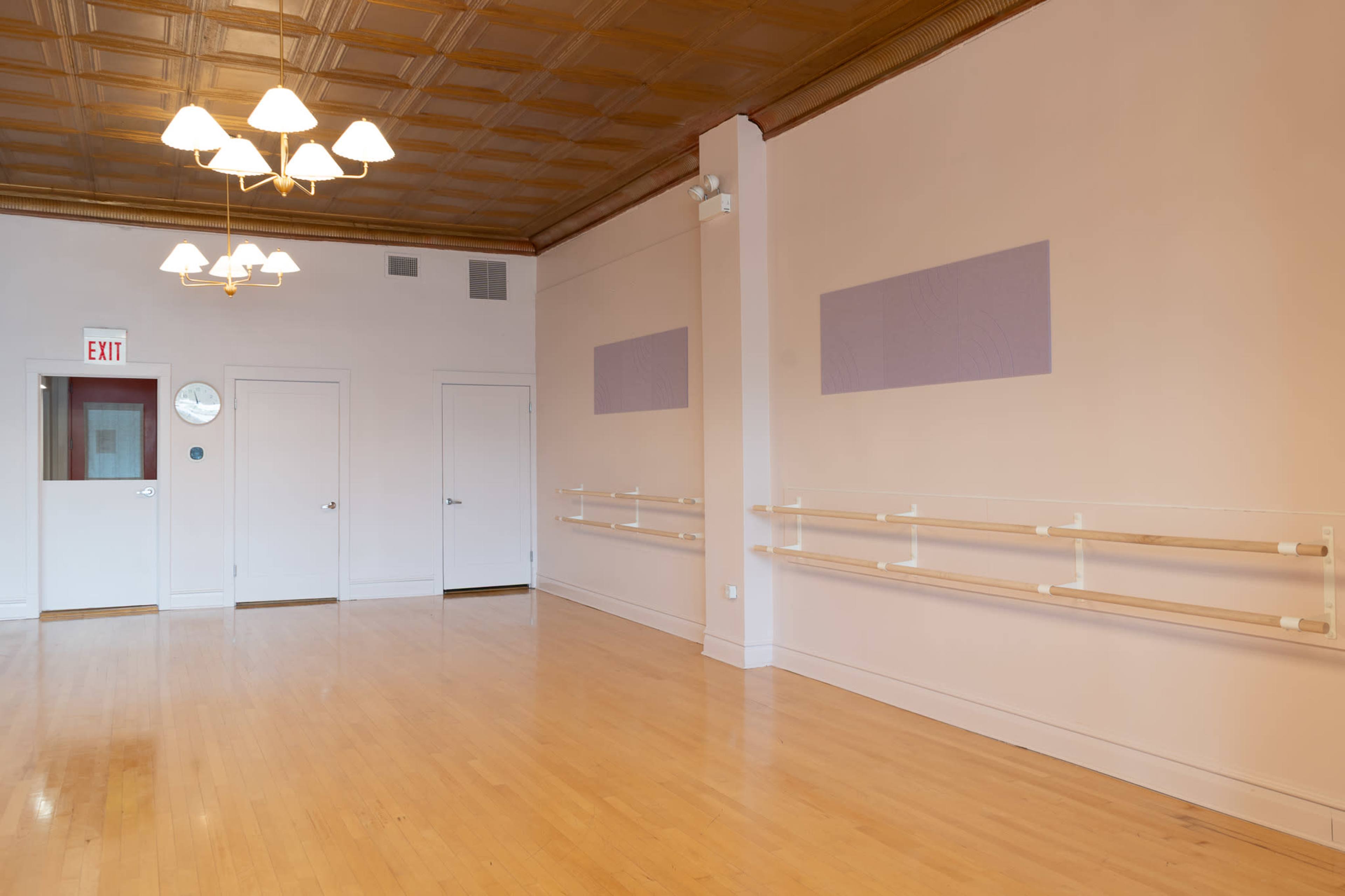 The image shows a spacious, empty dance studio with light wooden floors, wall-mounted ballet barres, and a decorative ceiling.