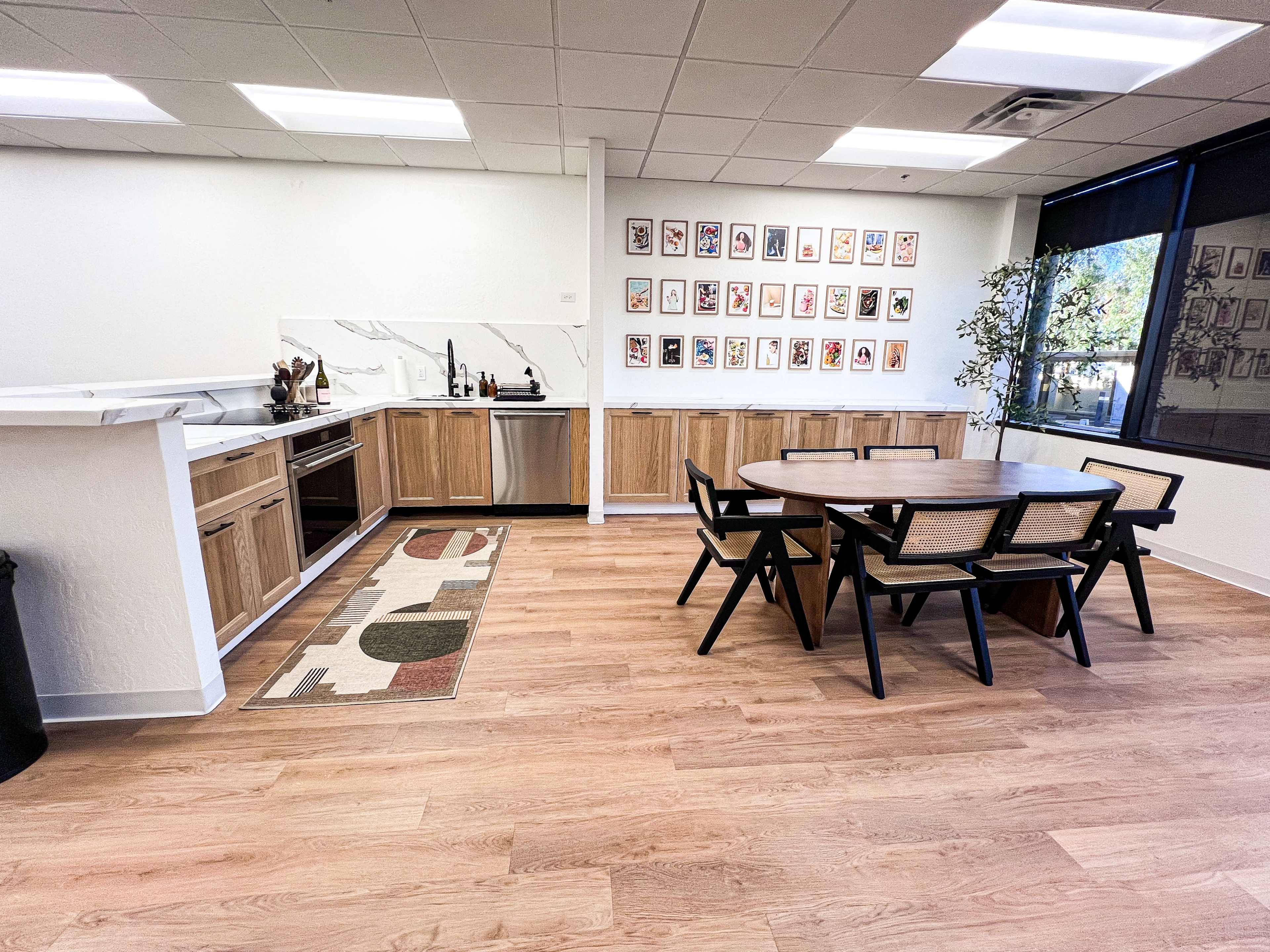A kitchen and dining area featuring wooden cabinetry, a modern table with black chairs, and wall art made up of framed pictures.