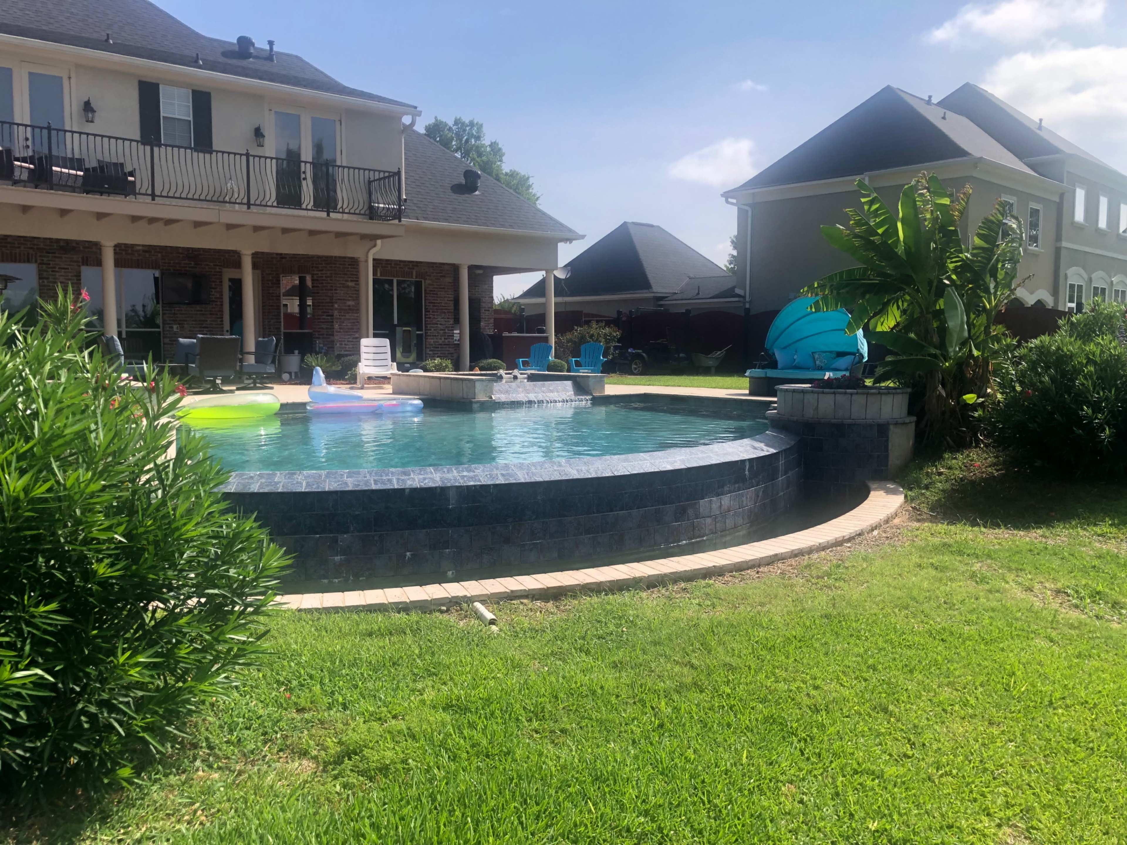 A backyard with a circular inground pool surrounded by green grass and lounge chairs, adjacent to a house with a patio.