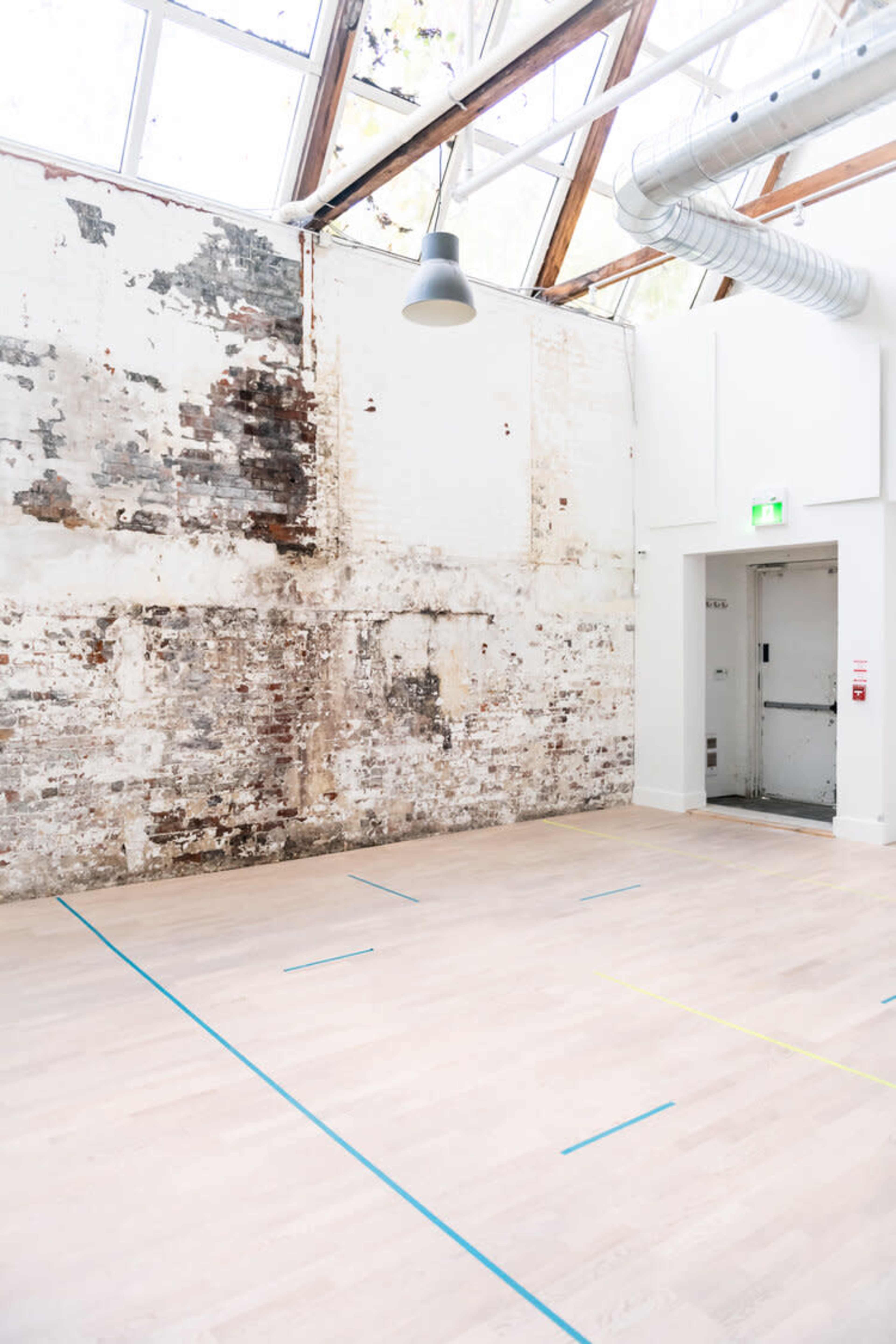 An empty indoor space with a weathered brick wall, wooden flooring, and a doorway.