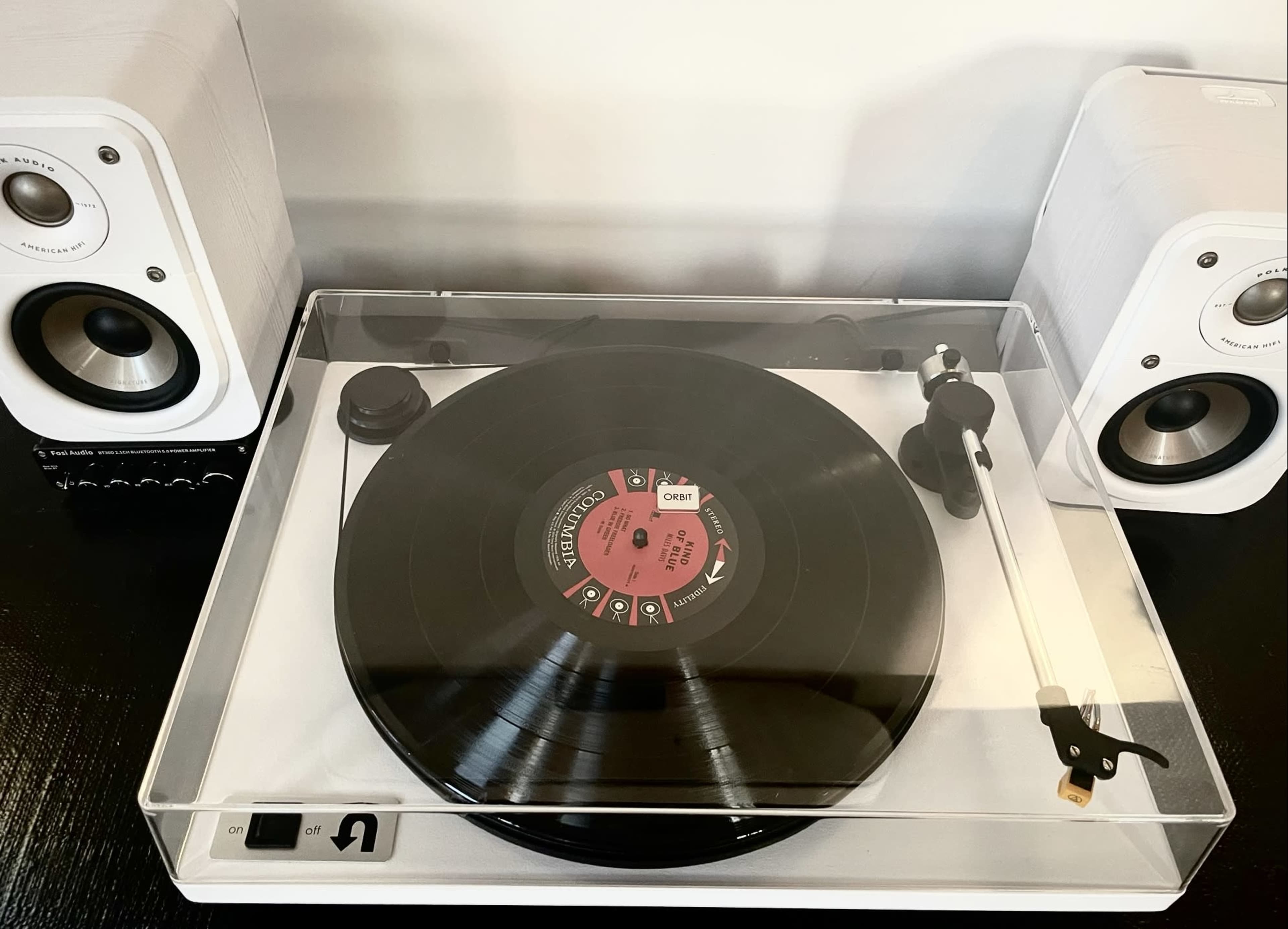 A record player is placed on a table with two speakers on either side, featuring a vinyl record positioned on the turntable.