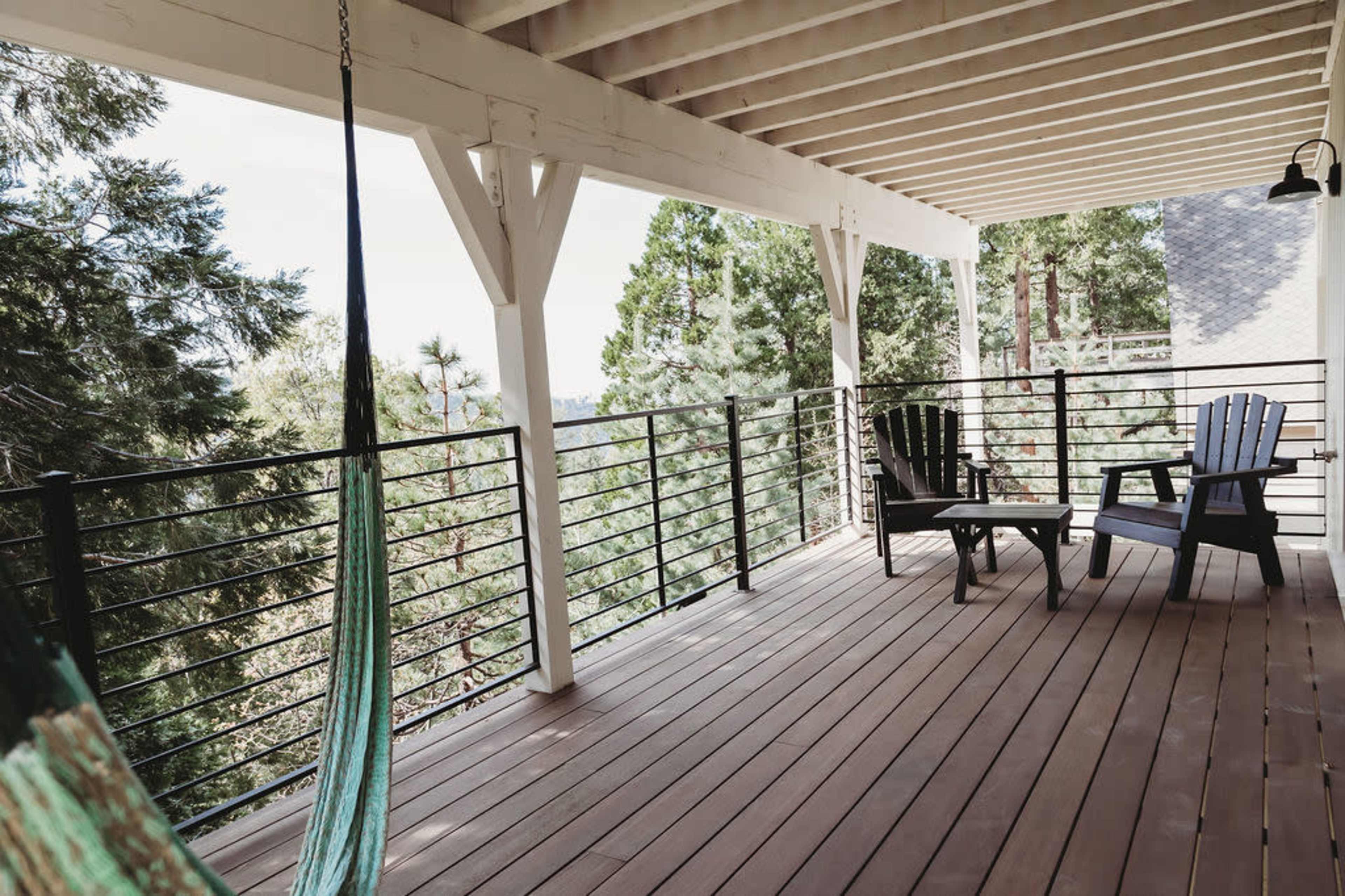 The image shows a wooden deck with two Adirondack chairs and a hammock, surrounded by trees and a railing overlooking a natural landscape.