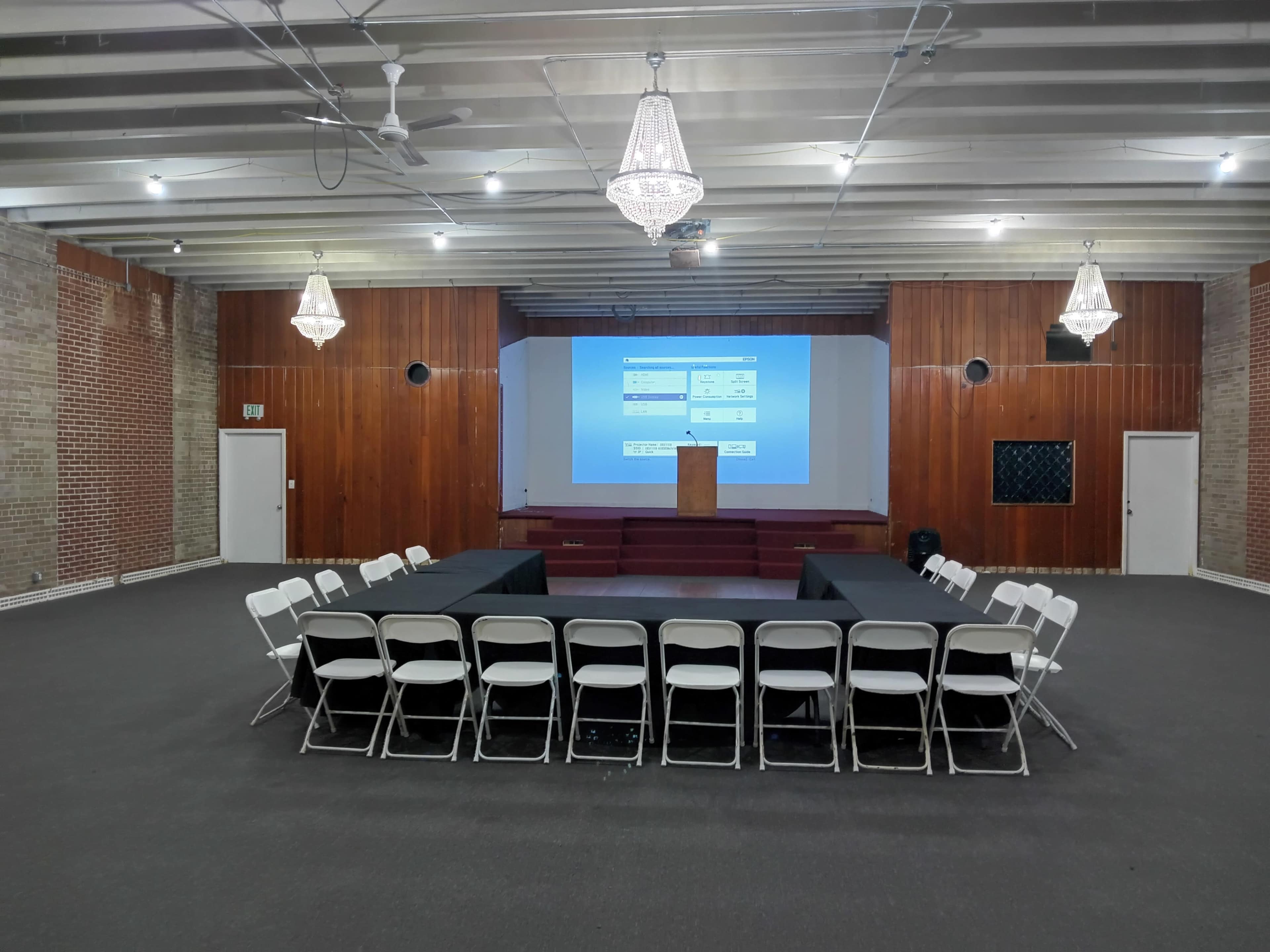 A conference room is arranged with a circular seating setup facing a presentation screen and a podium at the front.