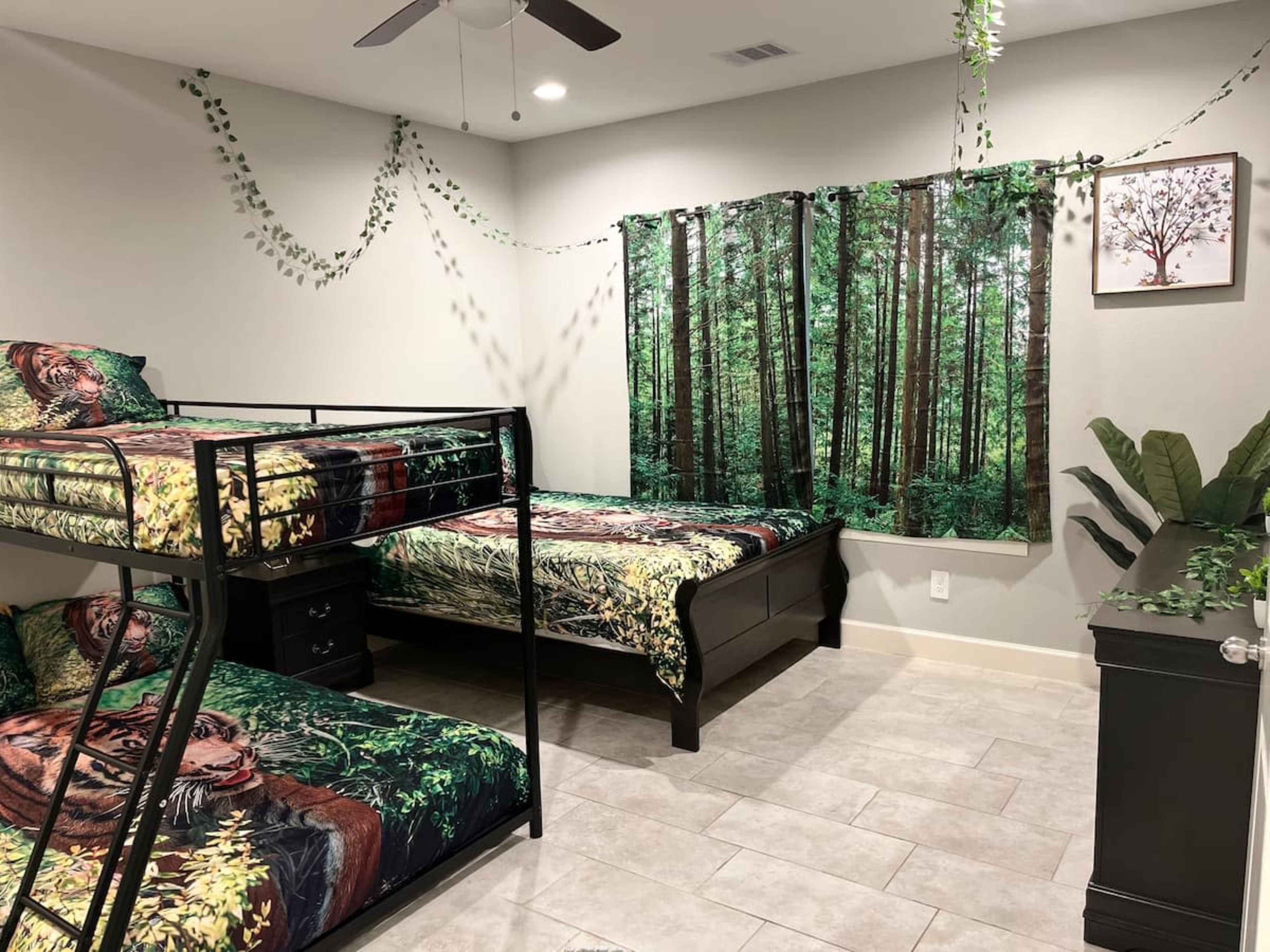 A bedroom featuring a bunk bed with nature-themed bedding, a double bed, a large forest-themed wall mural, and decorative plants.