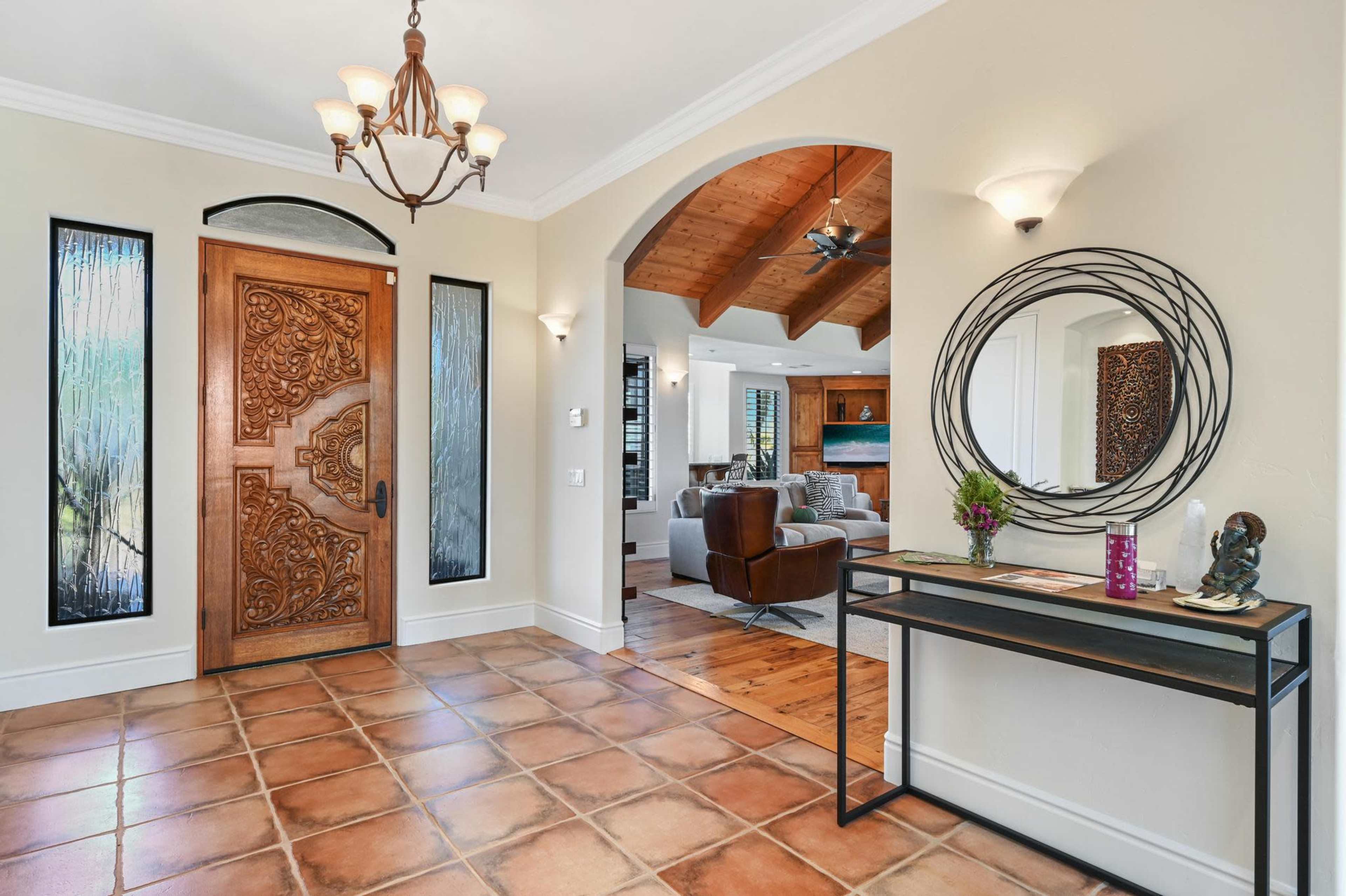 A spacious entryway with a decorative wooden door, ceramic tile flooring, a chandelier, and a console table against the wall.