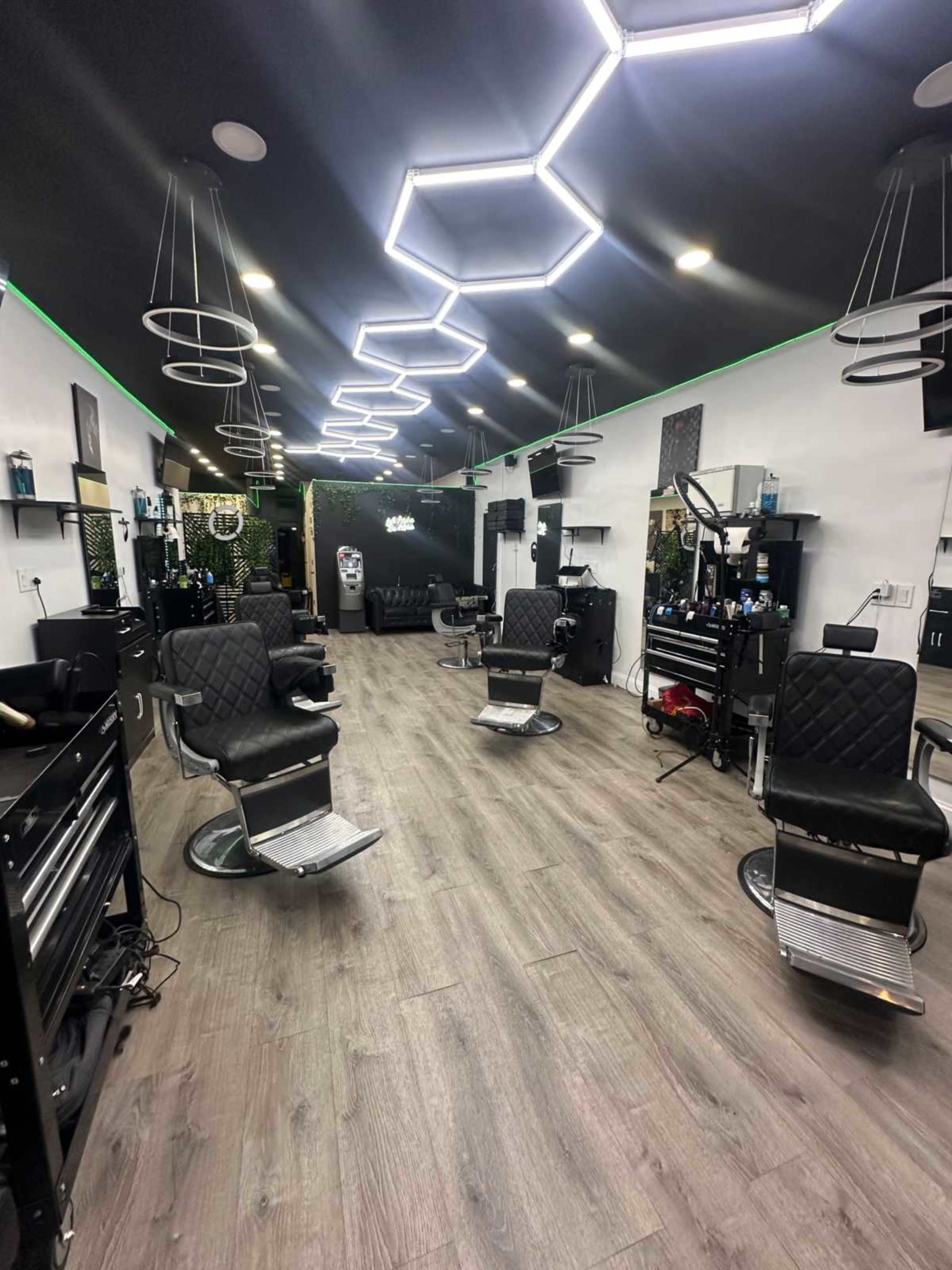A modern barbershop interior features multiple styling stations with black leather chairs and hexagonal light fixtures overhead.