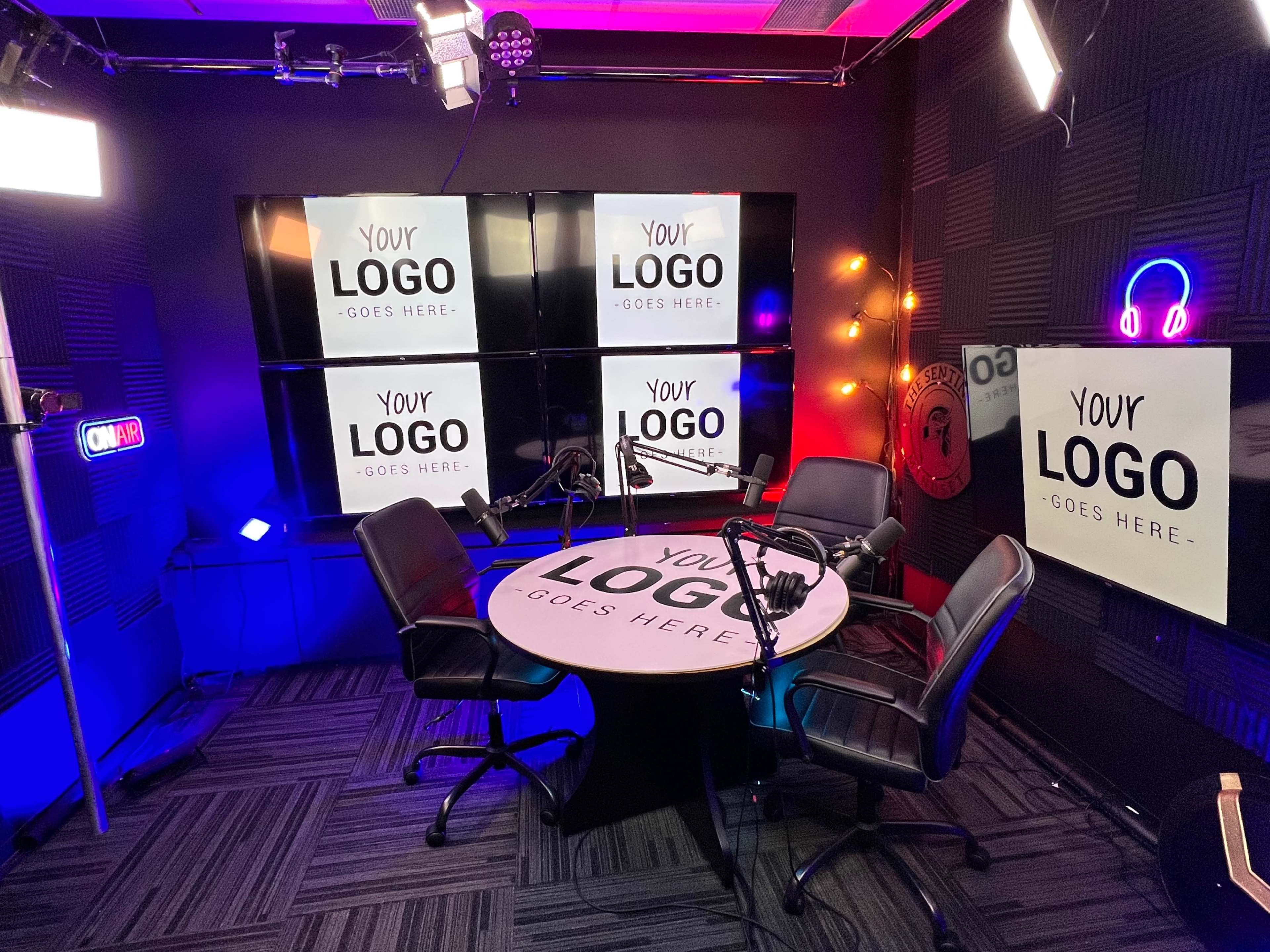 The image shows a podcast studio with a circular table, two black chairs, and multiple screens displaying the text "YOUR LOGO GOES HERE."