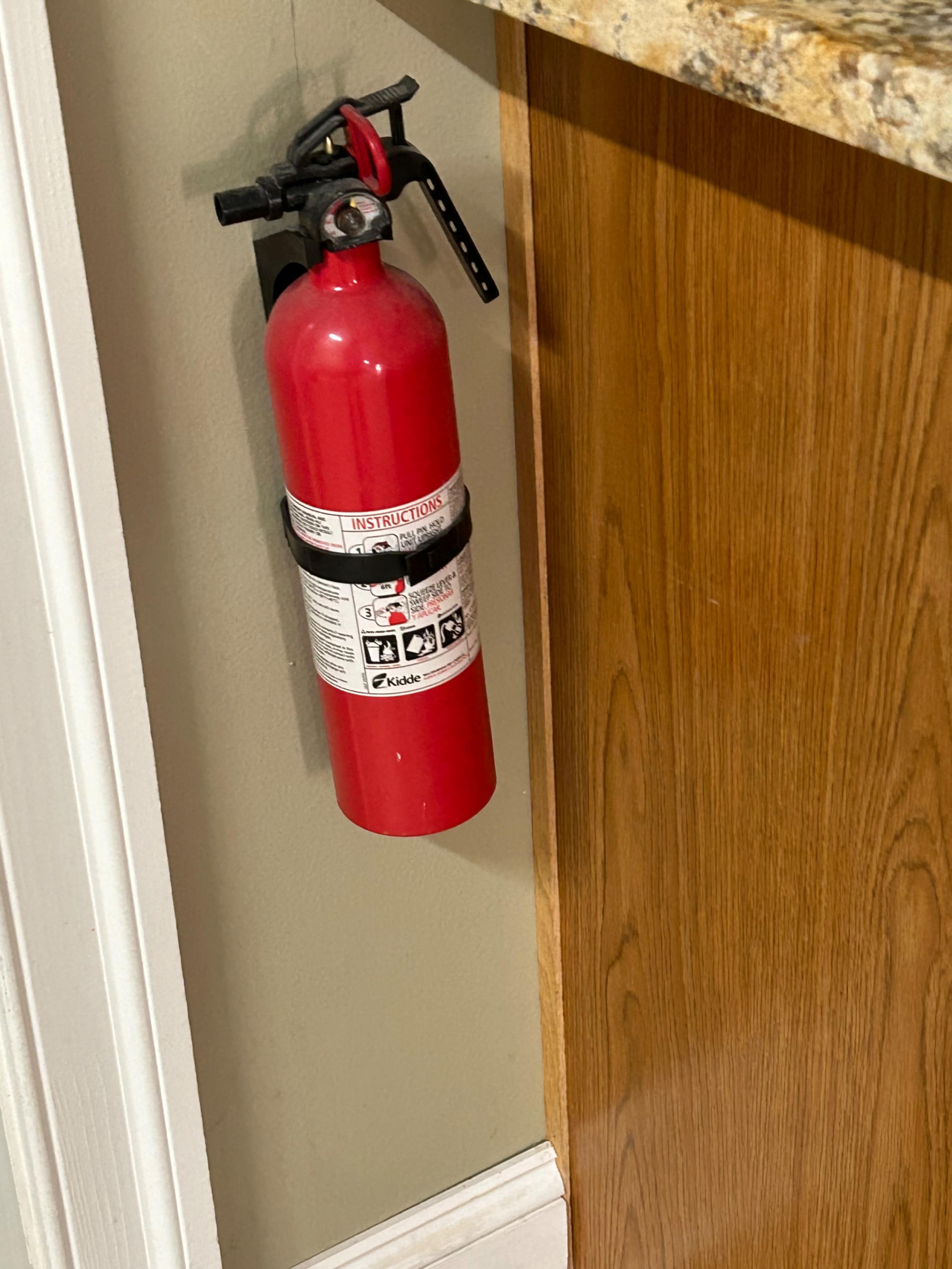 A red fire extinguisher is mounted on a wall next to a wooden cabinet.