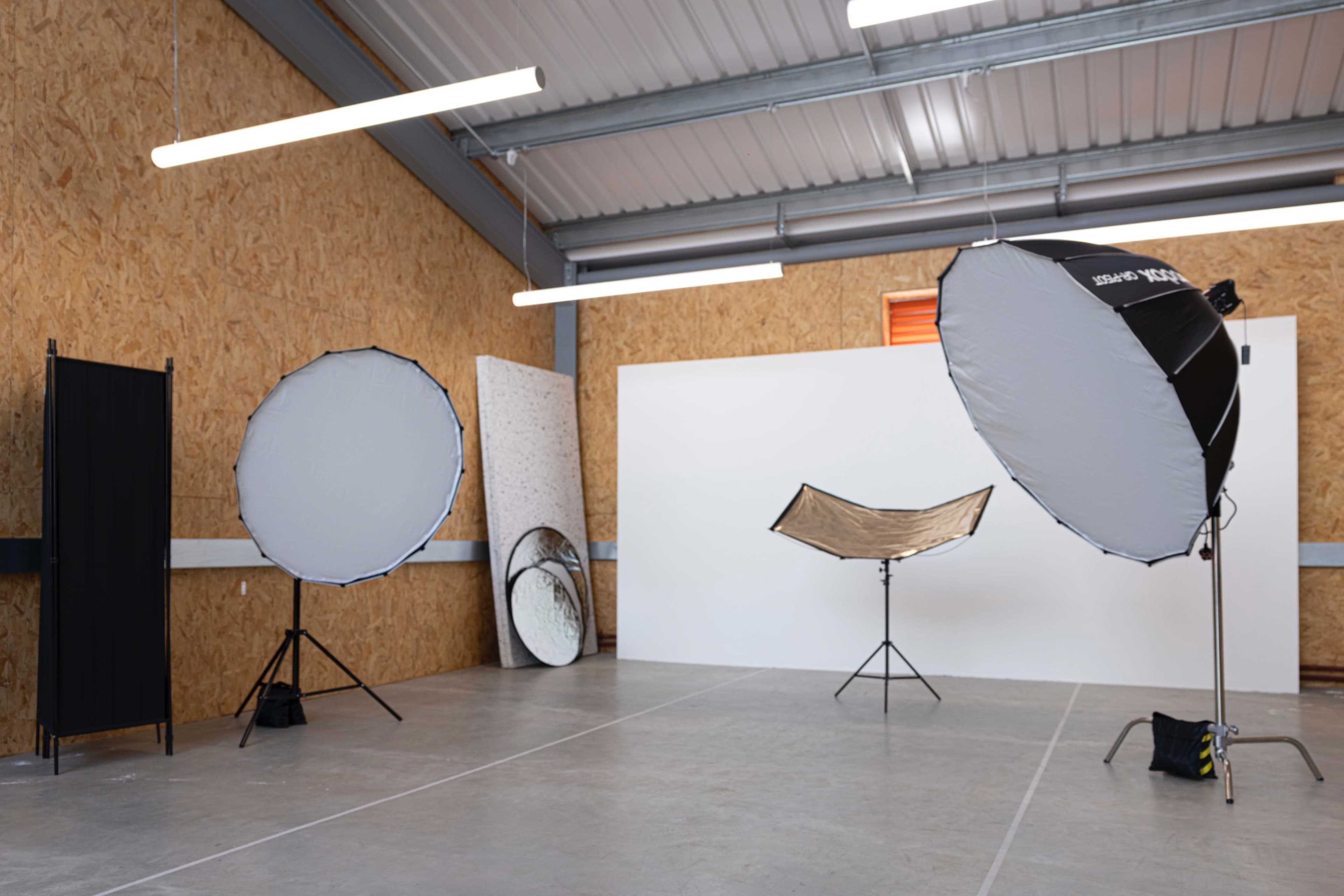 The image depicts a photography studio with two large softbox lights on stands, a reflector, and a neutral backdrop against an ornately textured wall.