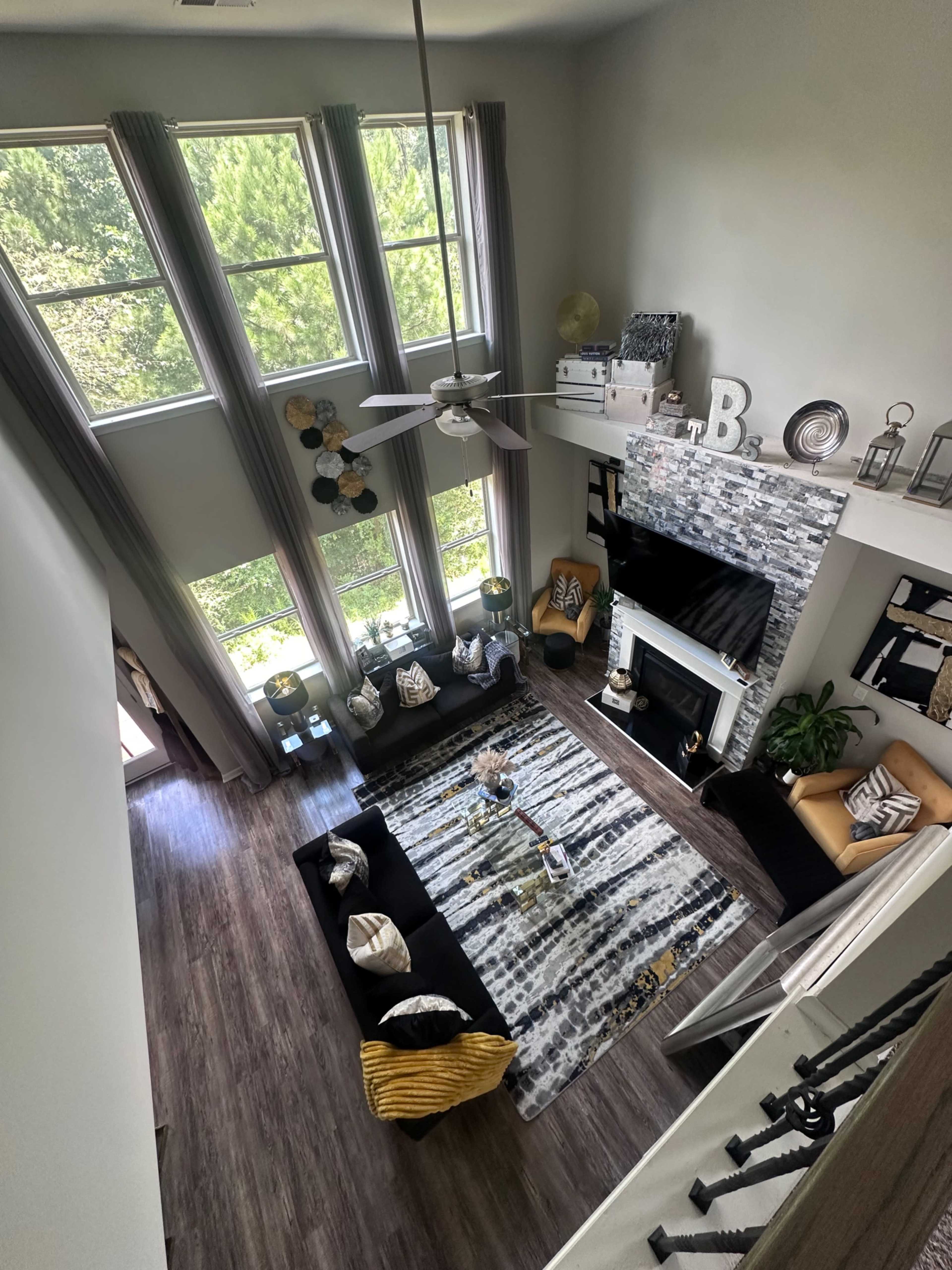 A spacious living room with tall windows, a patterned rug, and a fireplace, furnished with a mix of seating and decorative items.