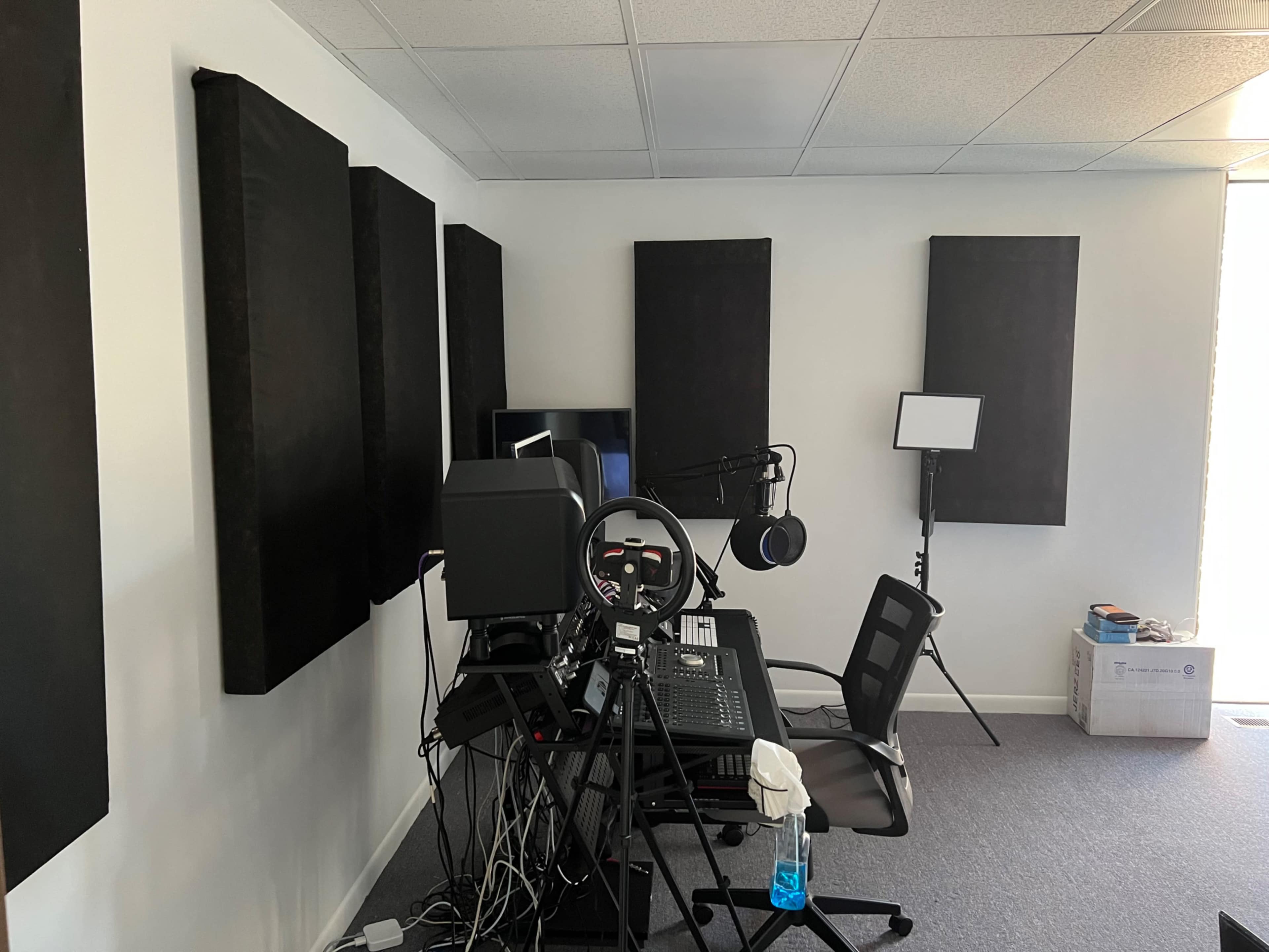 An audio recording studio with soundproofing panels on the walls, a desk with recording equipment, and a microphone setup.
