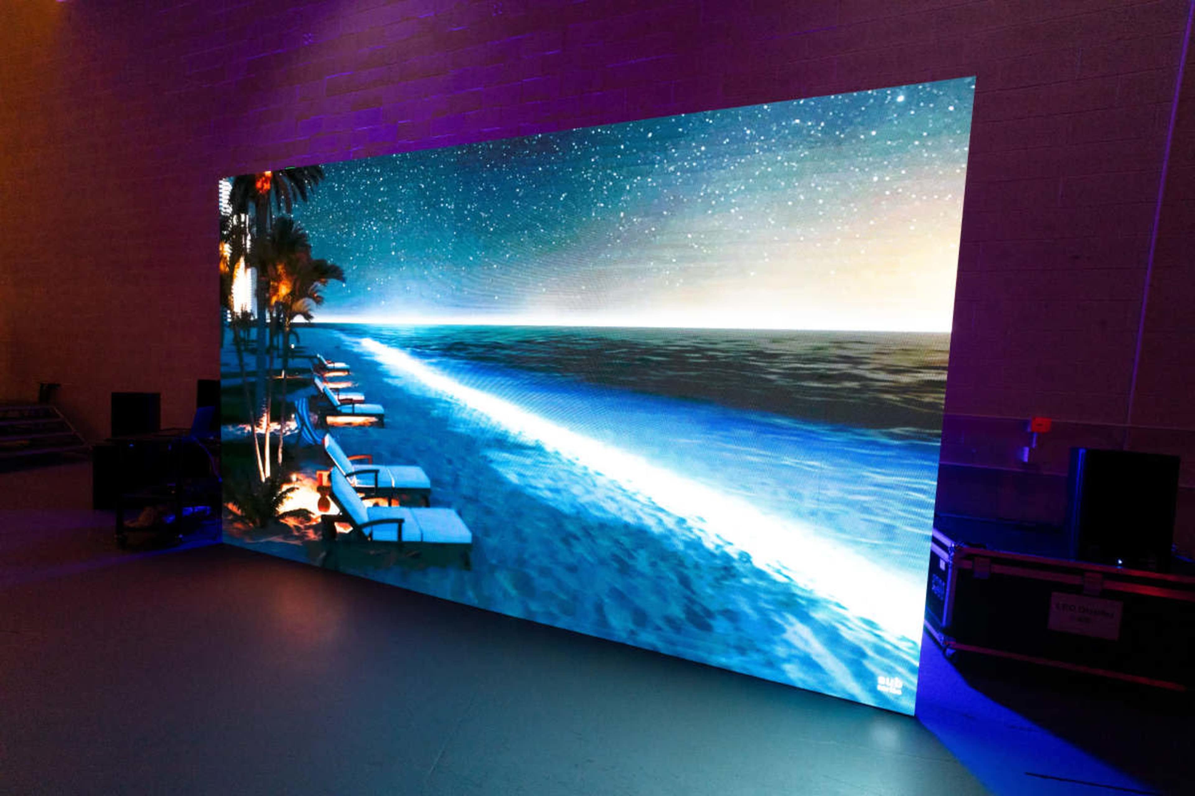 The image shows a large display screen depicting a serene beach scene at night, featuring lounge chairs and a starry sky over the ocean.