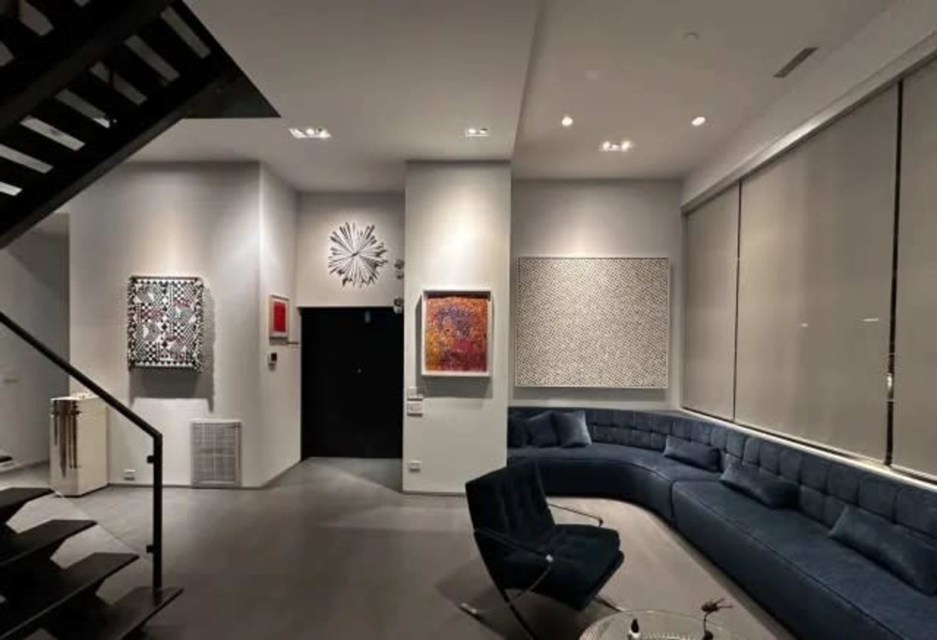 The image features a modern living space with a curved blue sectional sofa, abstract artwork on the walls, and a staircase leading to an upper level.