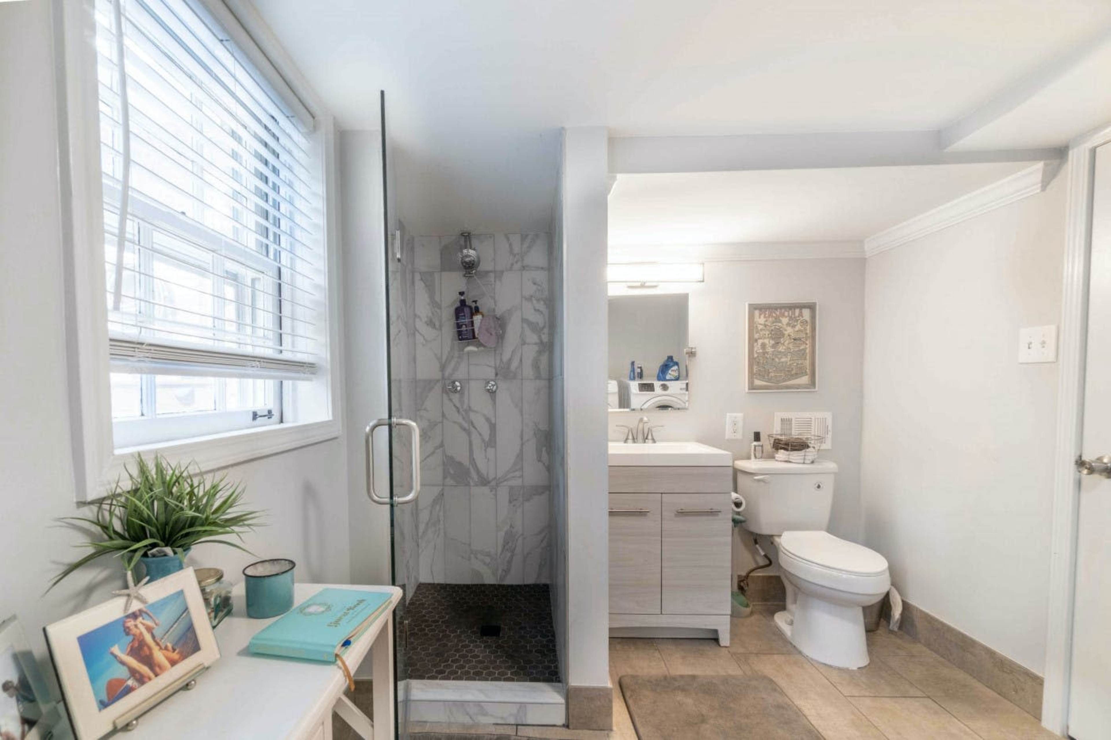 A modern bathroom featuring a glass shower, a vanity with a mirror, a toilet, and natural light from a window.