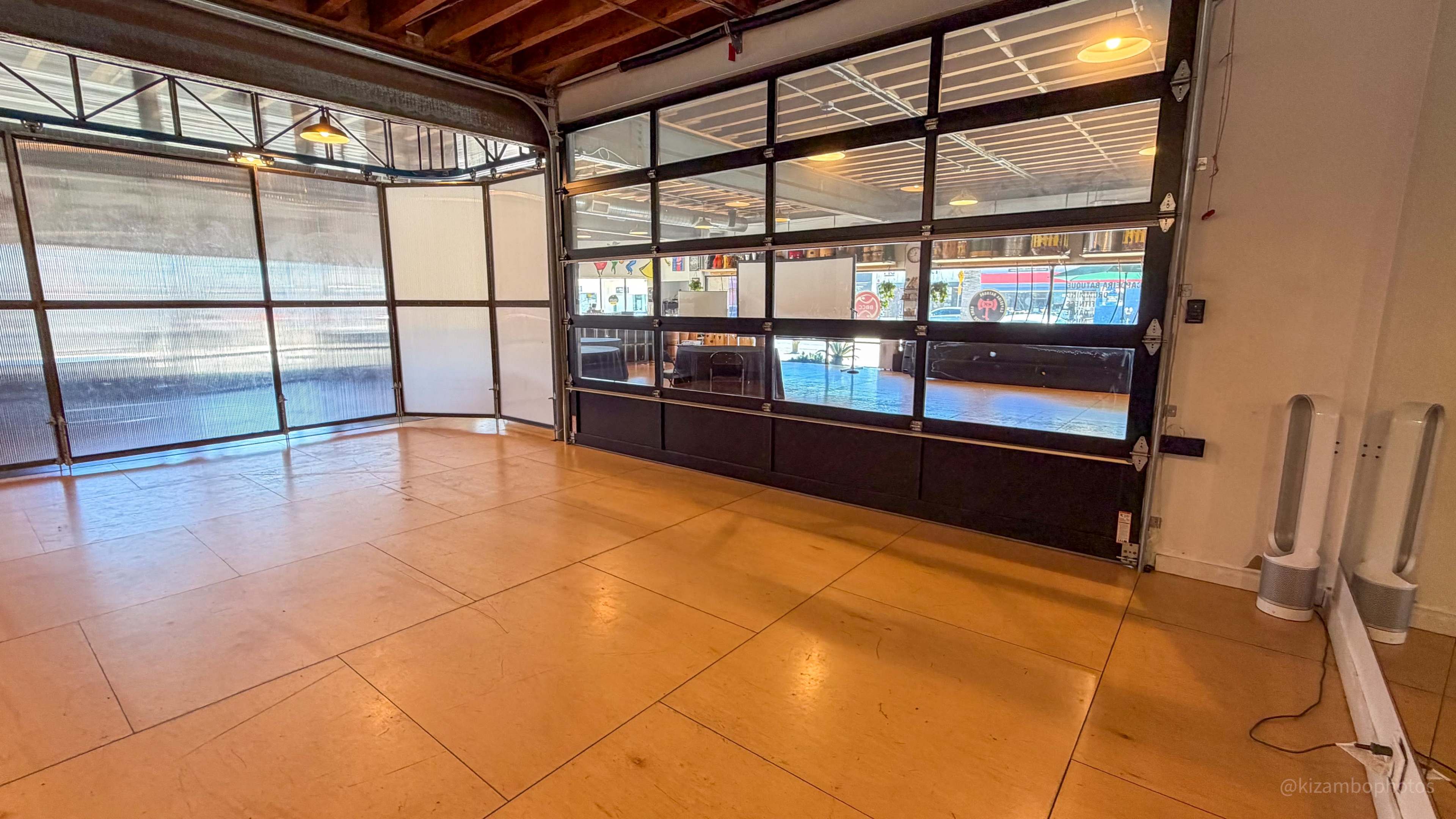 The image shows an open space with a large glass garage door and wooden flooring, illuminated by natural light from outside.