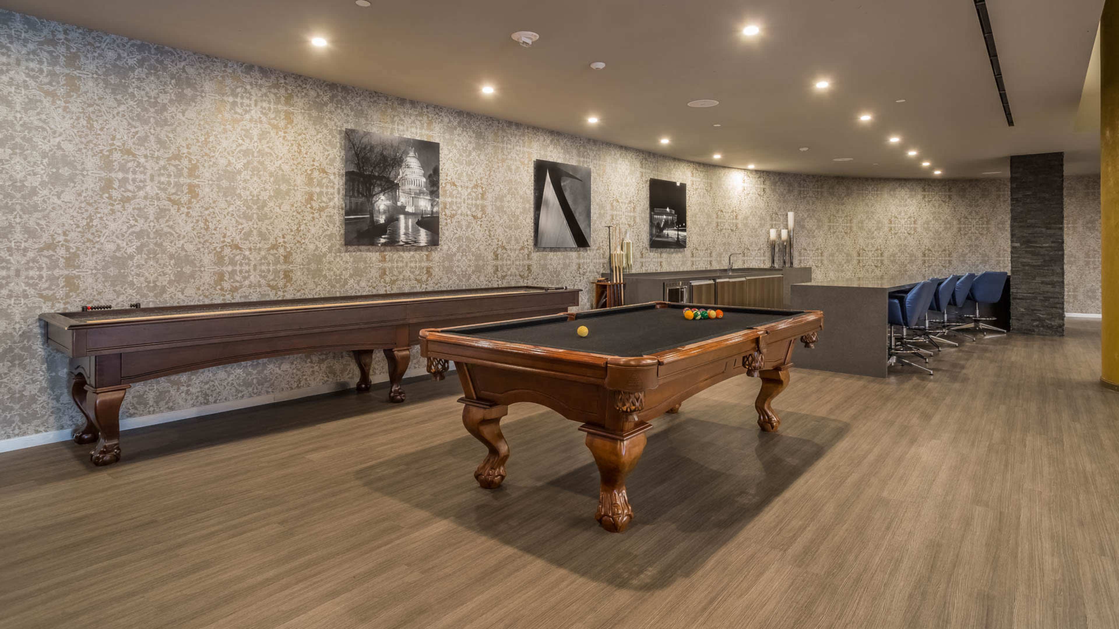 A modern game room featuring a pool table, a decorative wall, and a bar-style seating area with high chairs.
